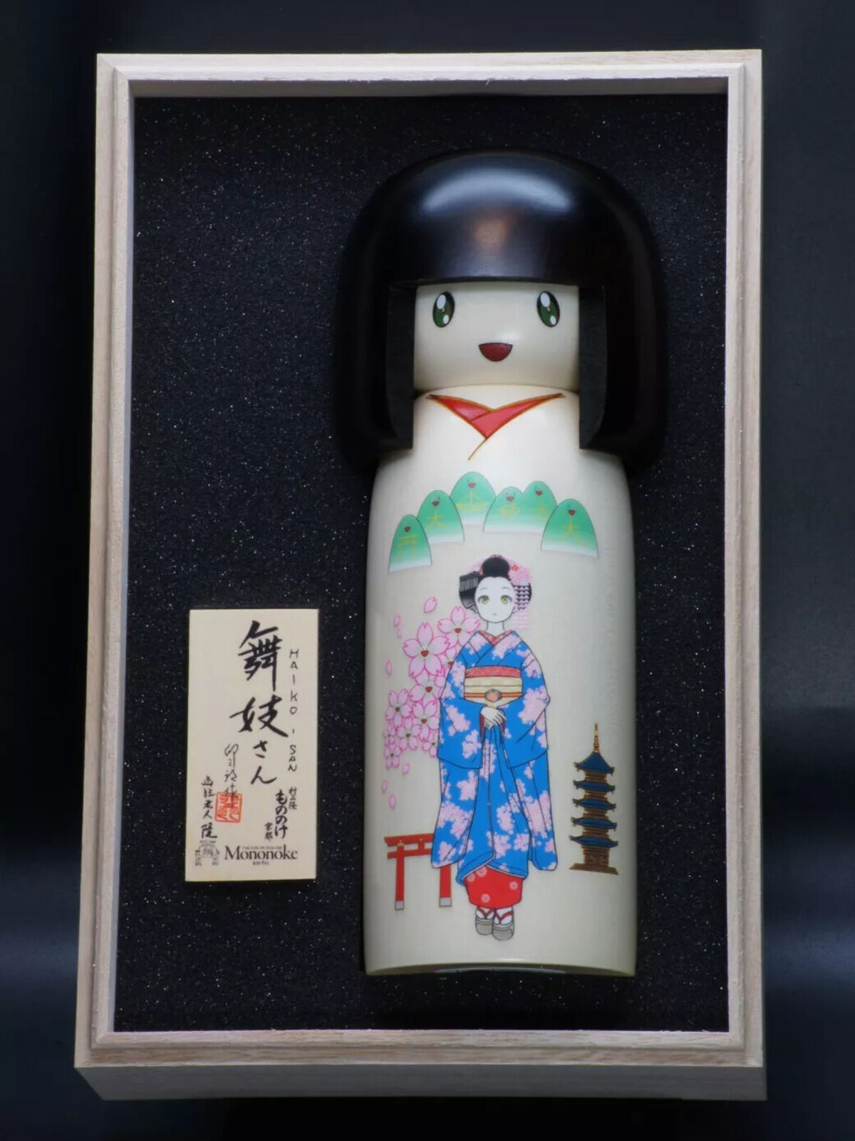 A wooden doll in a wooden box with a picture of a woman in a kimono.