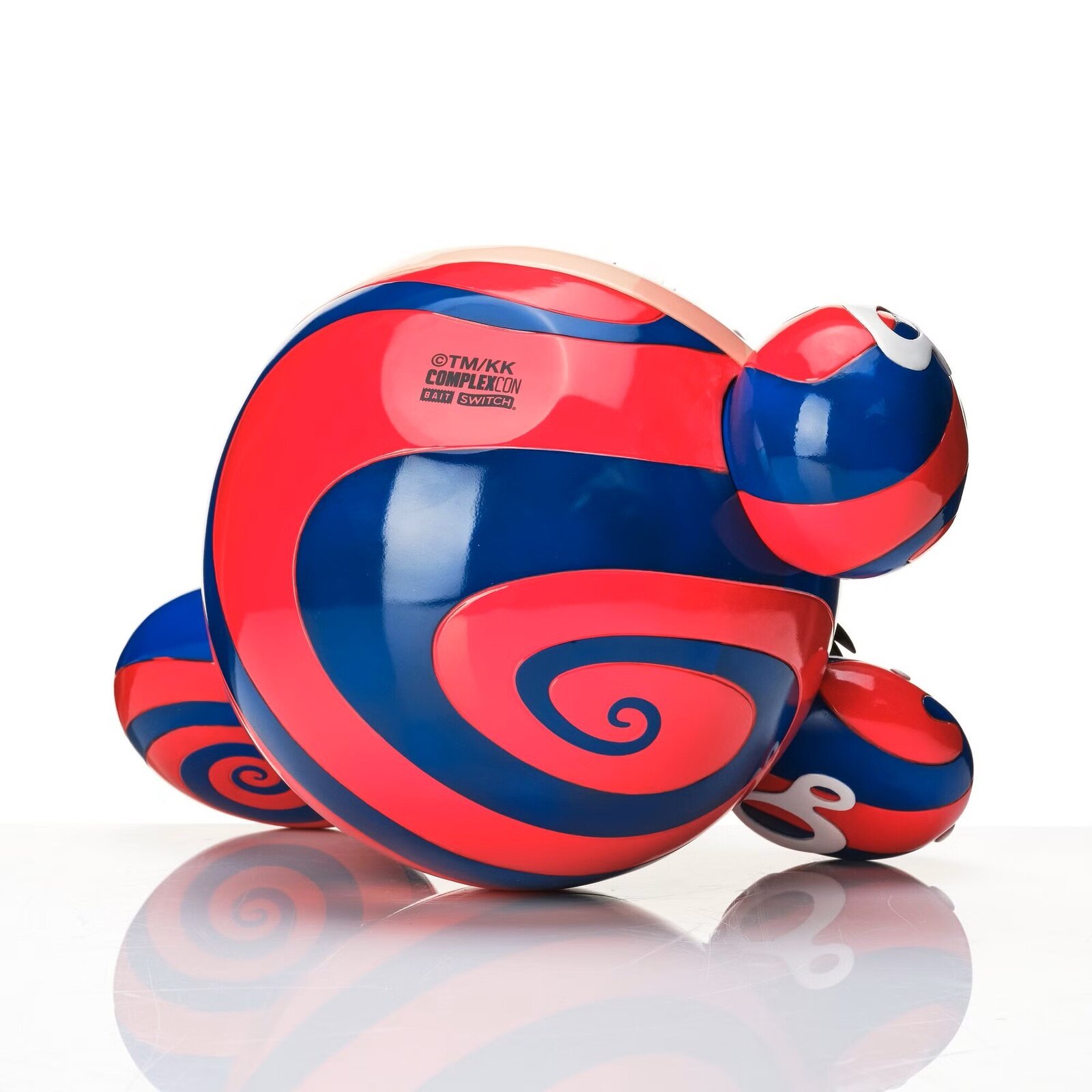 A colorful, cartoonish figure with a large mouth and spiral eye sits beside its matching box.