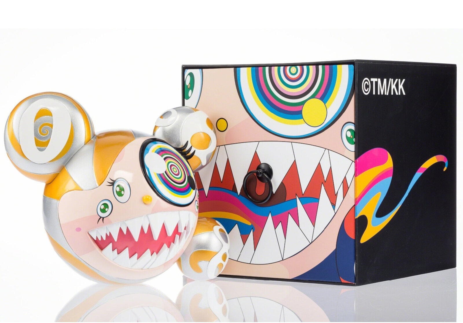 A colorful, stylized figure with a wide grin and spiral eyes sits beside its matching box.