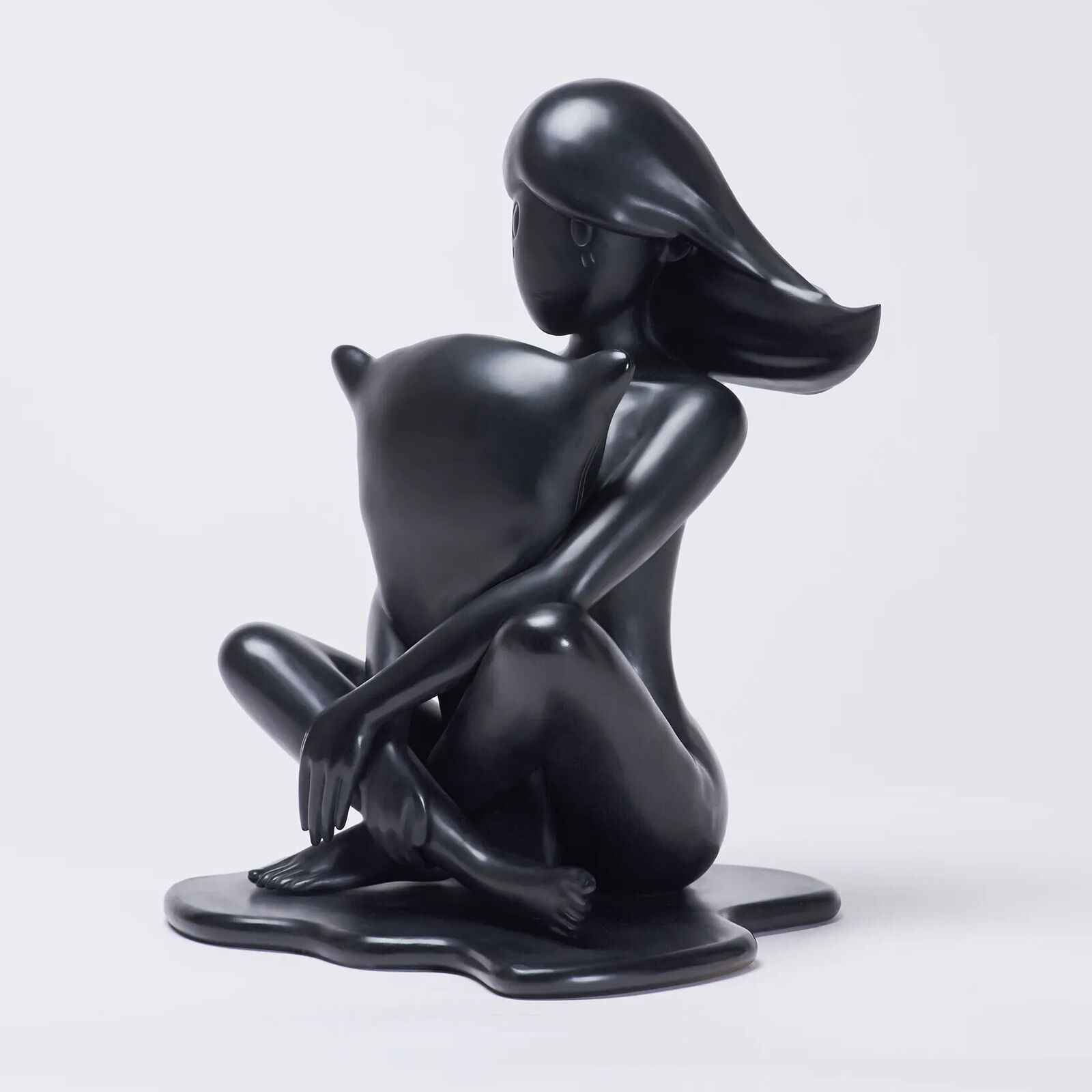 A black sculpture of a woman sitting on the ground.