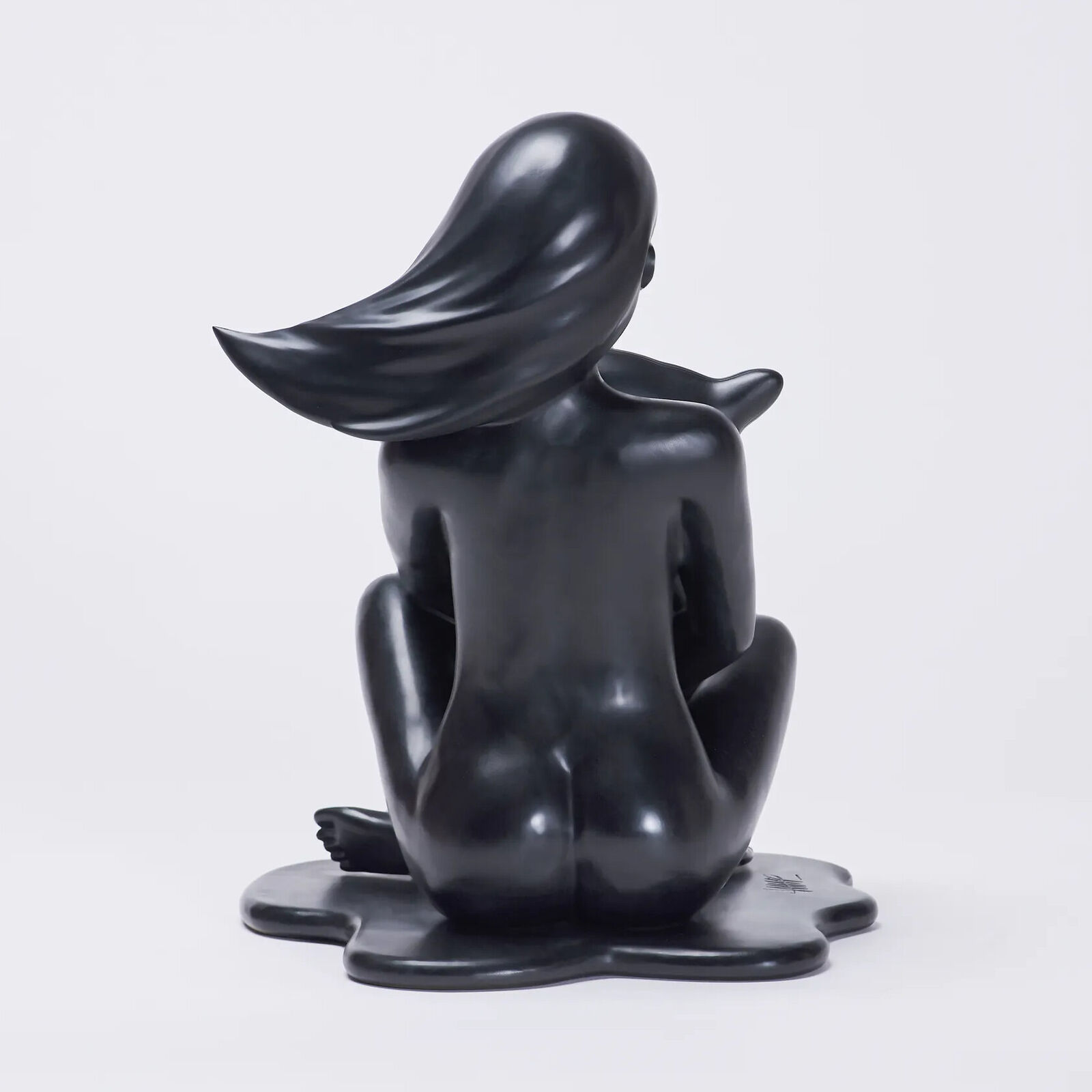 A black sculpture of a woman sitting on the ground.