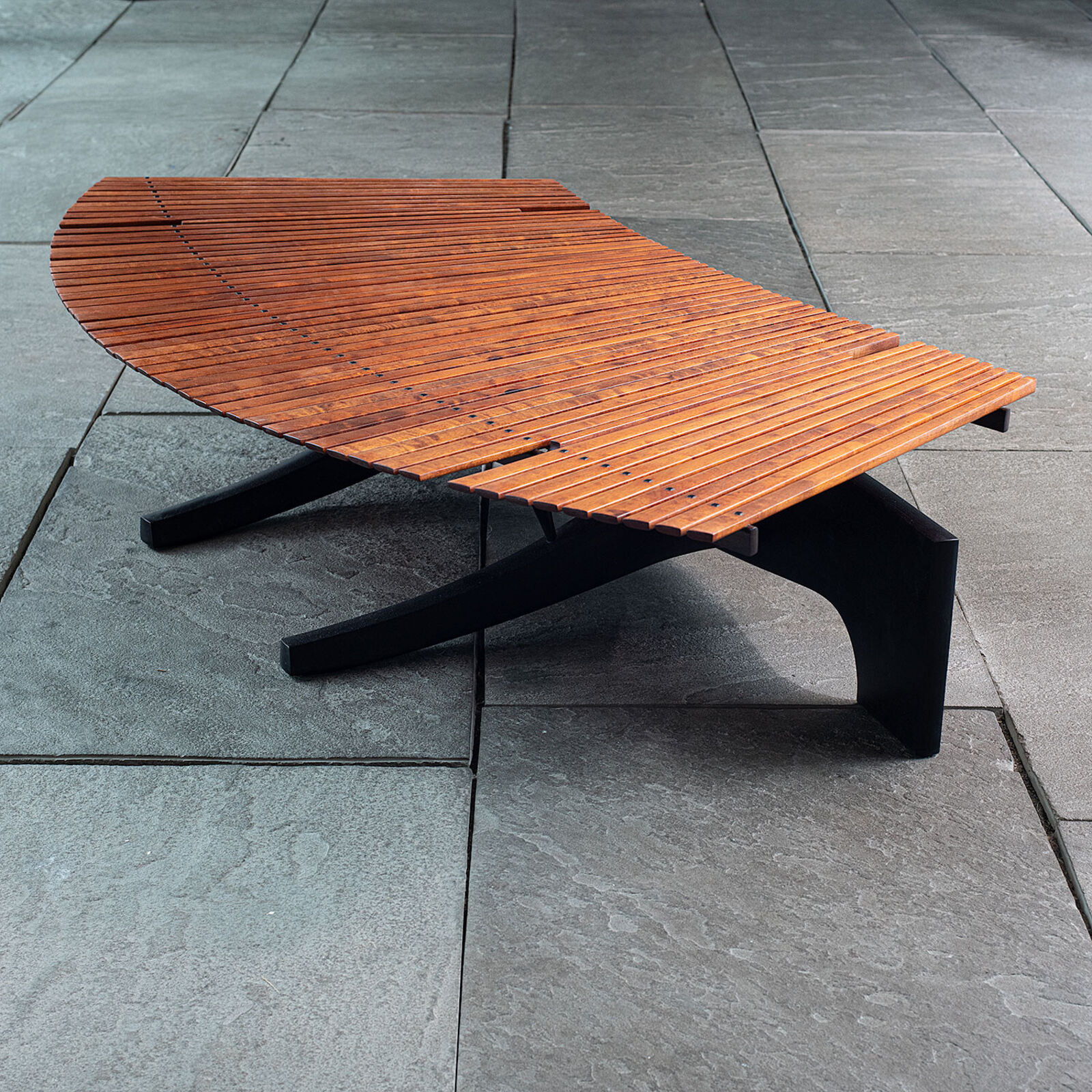 A modern wooden coffee table with a curved slatted top and sculpted black legs.
