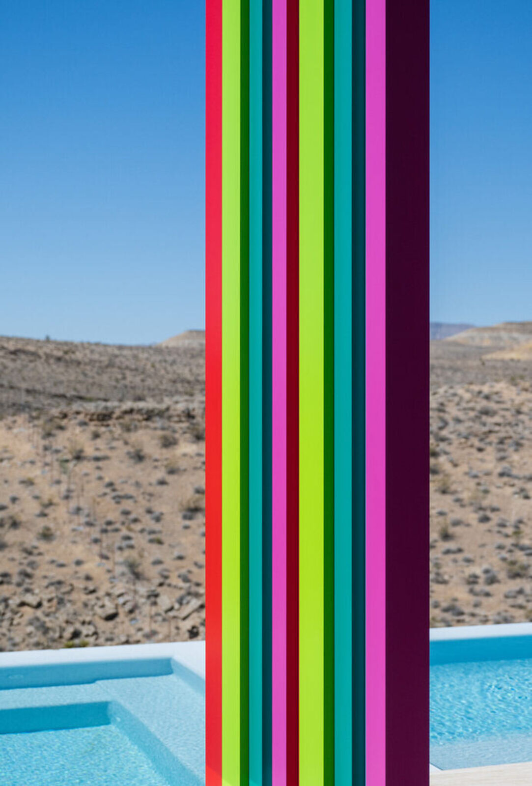A tall, colorful striped sculpture stands in a desert landscape.