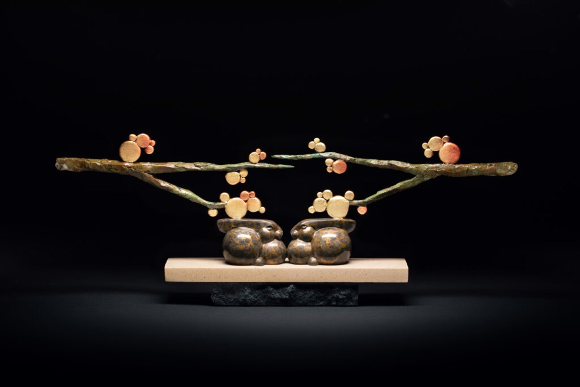 A sculpture of two rabbits sitting on a branch of a tree.