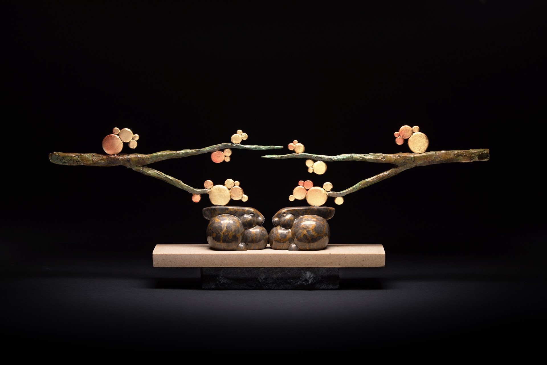 A sculpture of two rabbits sitting on a branch of a tree.