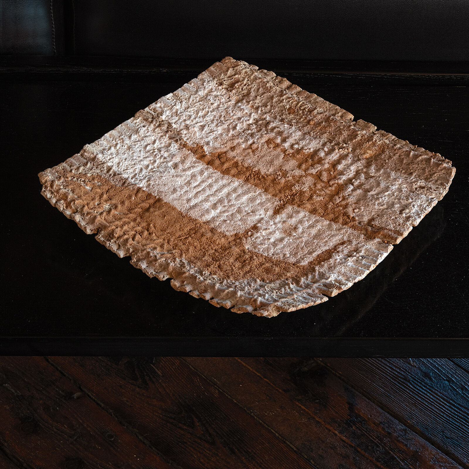 A textured, rectangular ceramic dish with a rough, uneven surface resting on a dark table.