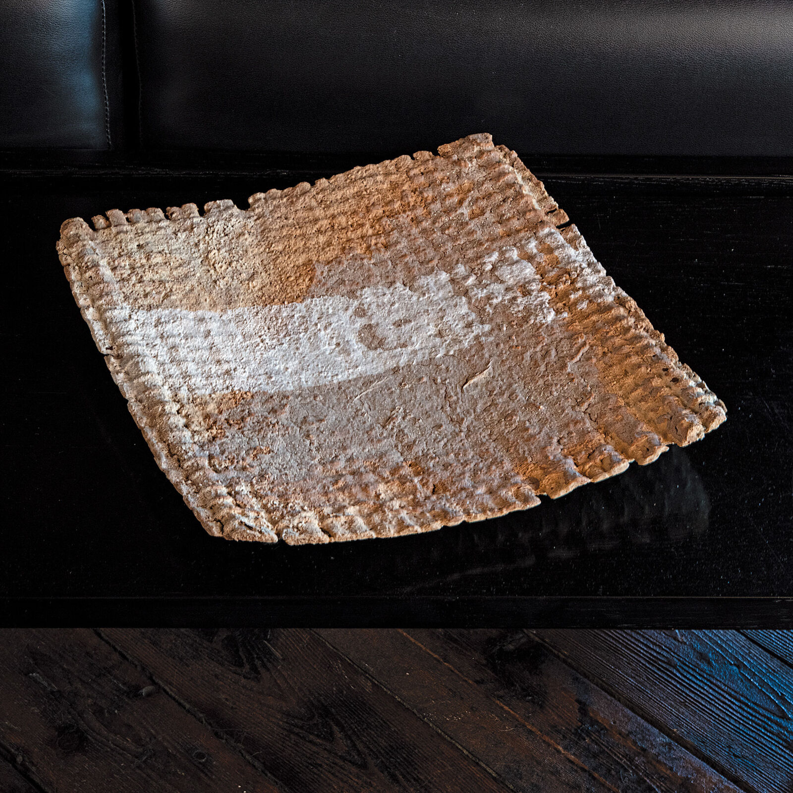 A matzoh on a black table on a wooden floor.