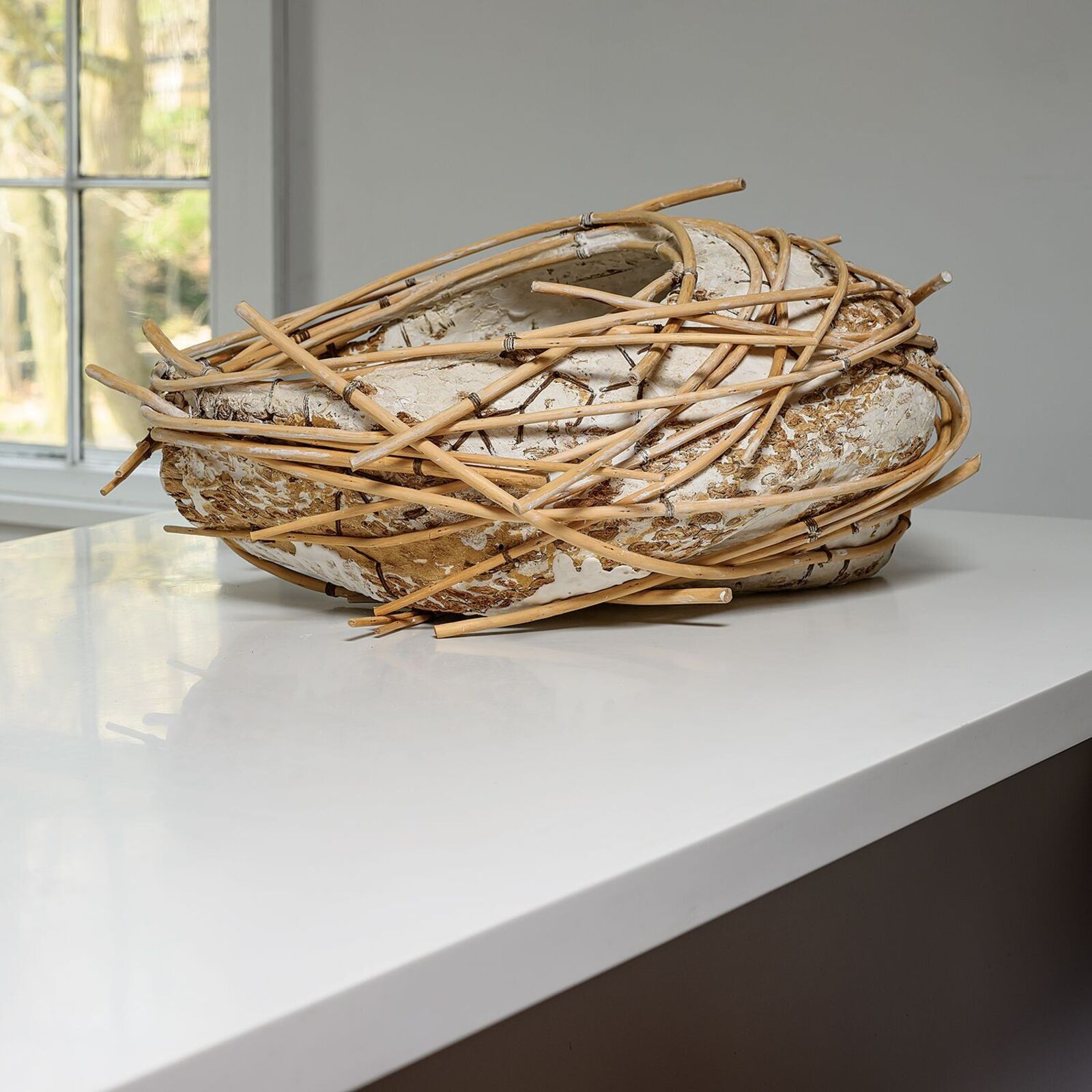 A rustic sculpture resembling a bird's nest made from woven bamboo and textured clay.