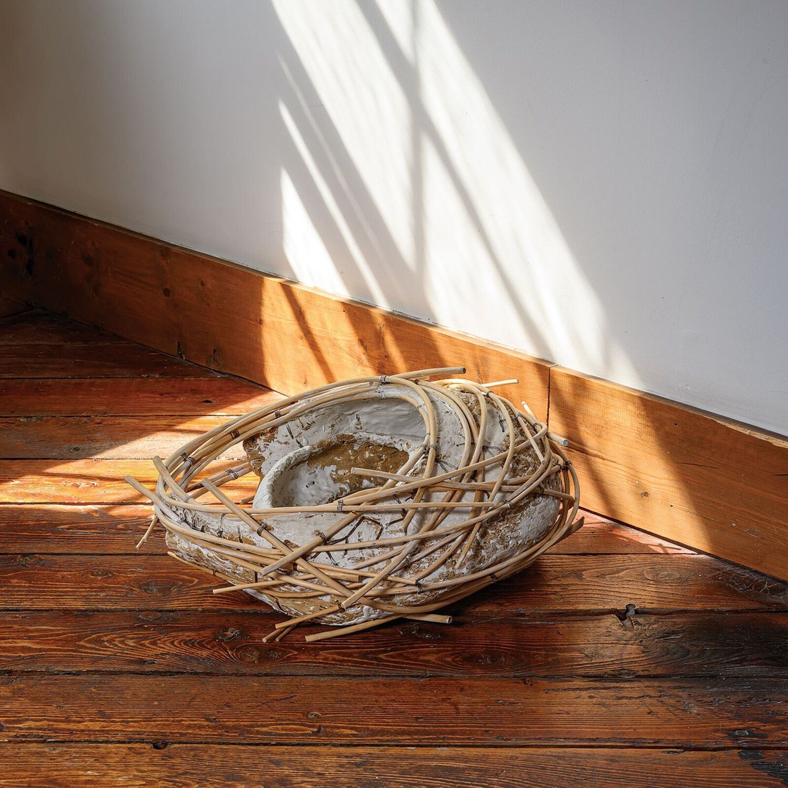 A rustic sculpture resembling a bird's nest made from woven bamboo and textured clay.