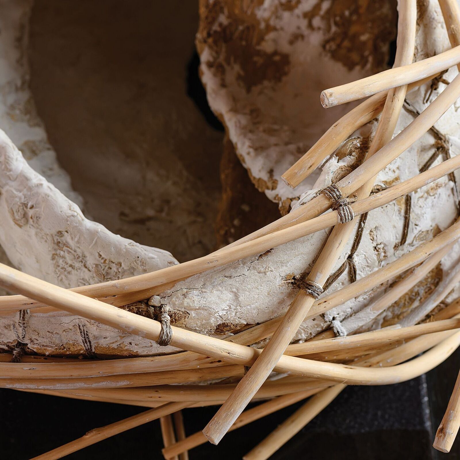 A rustic sculpture resembling a bird's nest made from woven bamboo and textured clay.