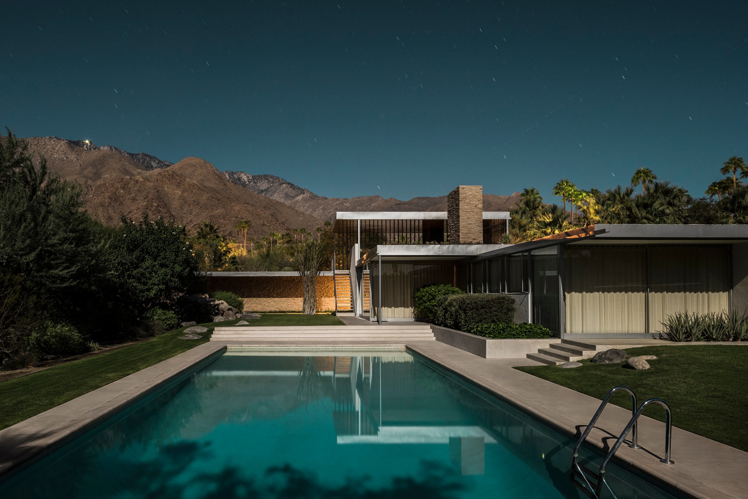 A swimming pool in front of a house with mountains in the background.