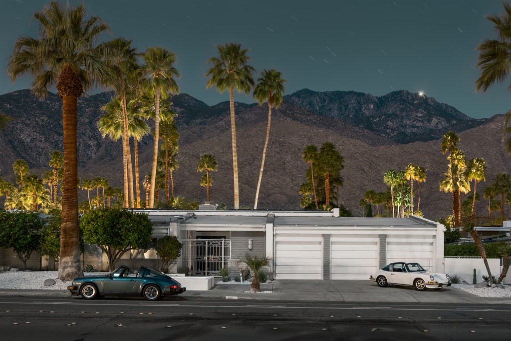 Two cars parked in front of a house with palm trees.