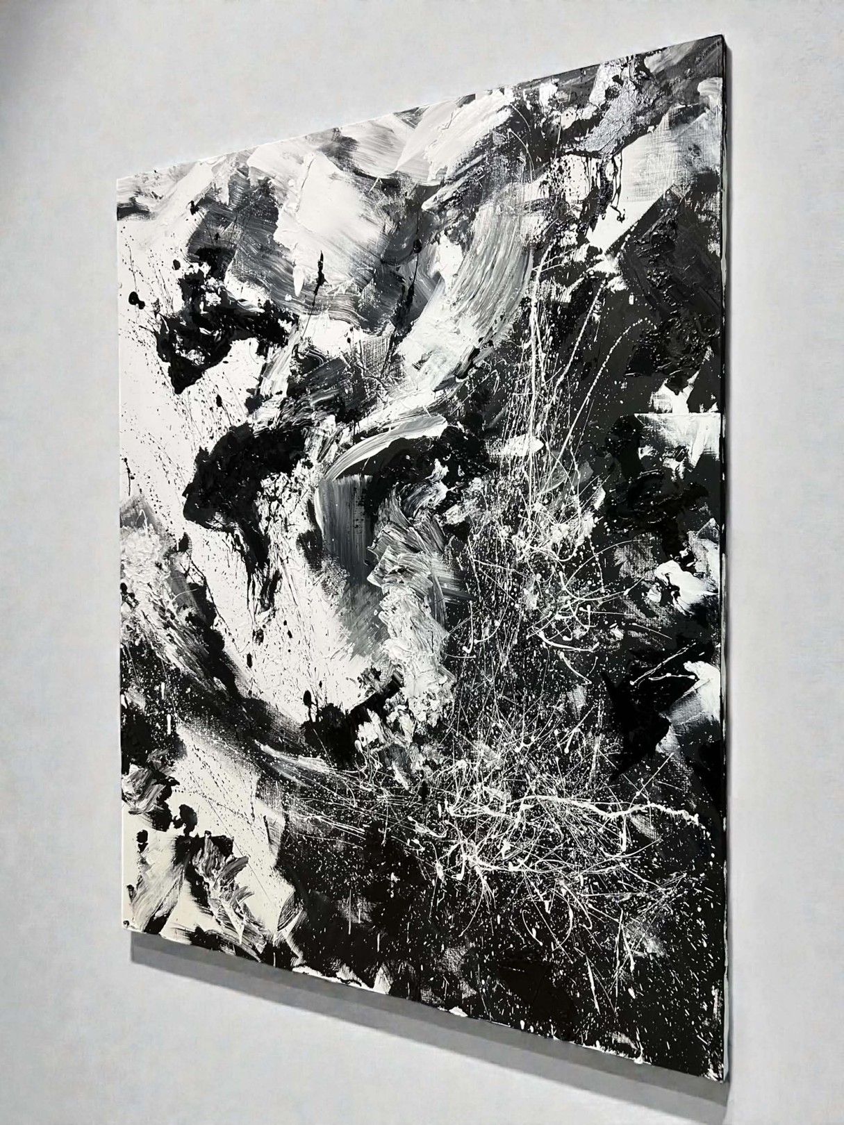 A dynamic black and white abstract painting featuring bold brushstrokes, splatters, and textured layers.