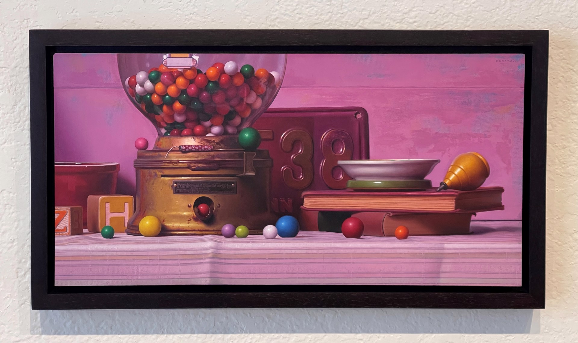 A colorful still life featuring a vintage gumball machine, books, and scattered spheres against a soft pink backdrop.