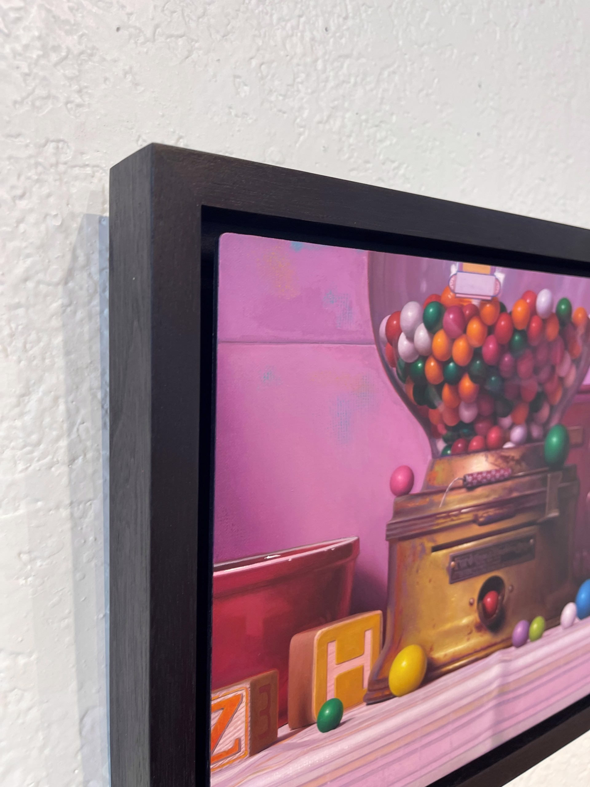 A colorful still life featuring a vintage gumball machine, books, and scattered spheres against a soft pink backdrop.