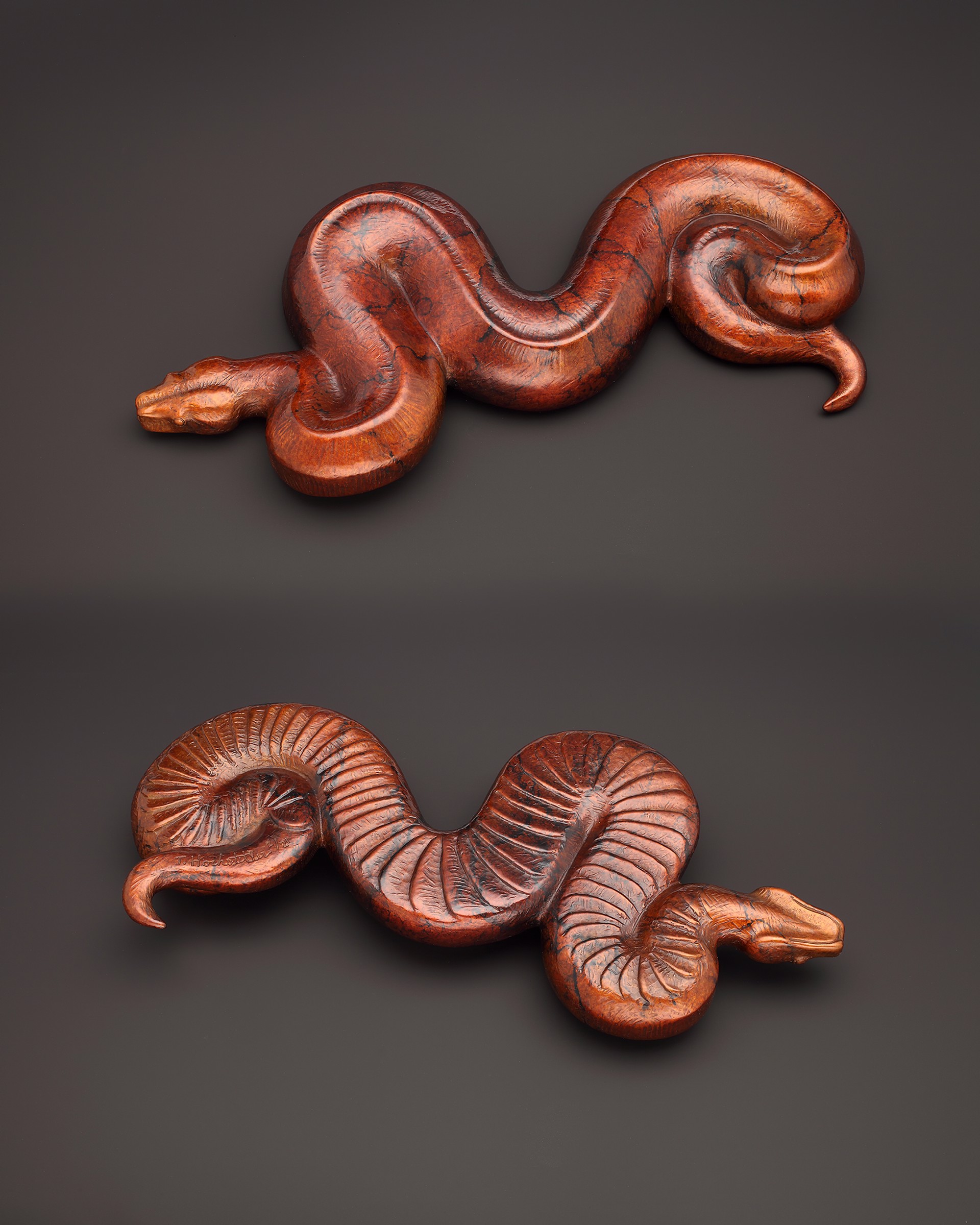 A pair of carved wooden snakes on a black background.