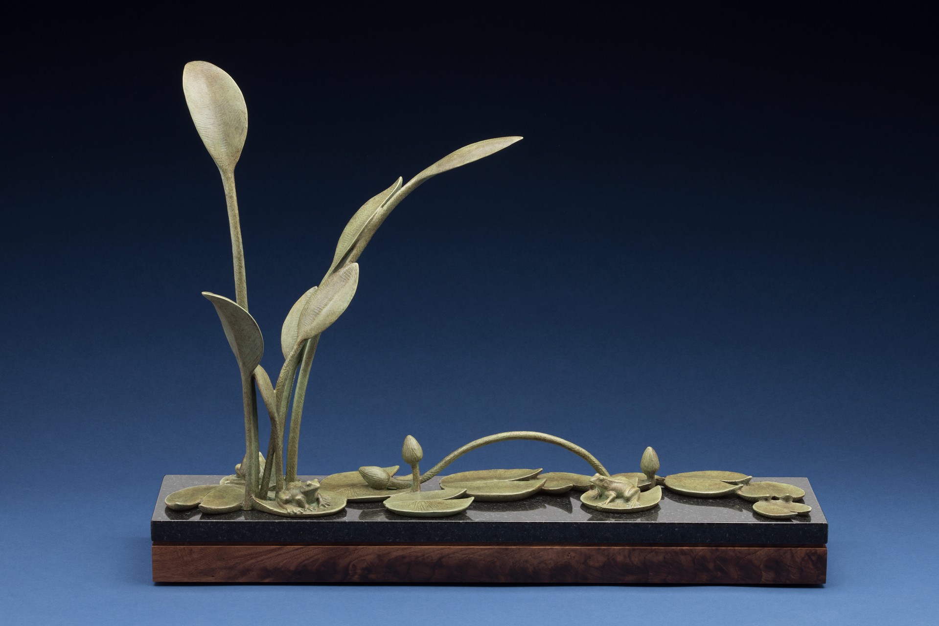 A bronze sculpture of a plant on a wooden base.
