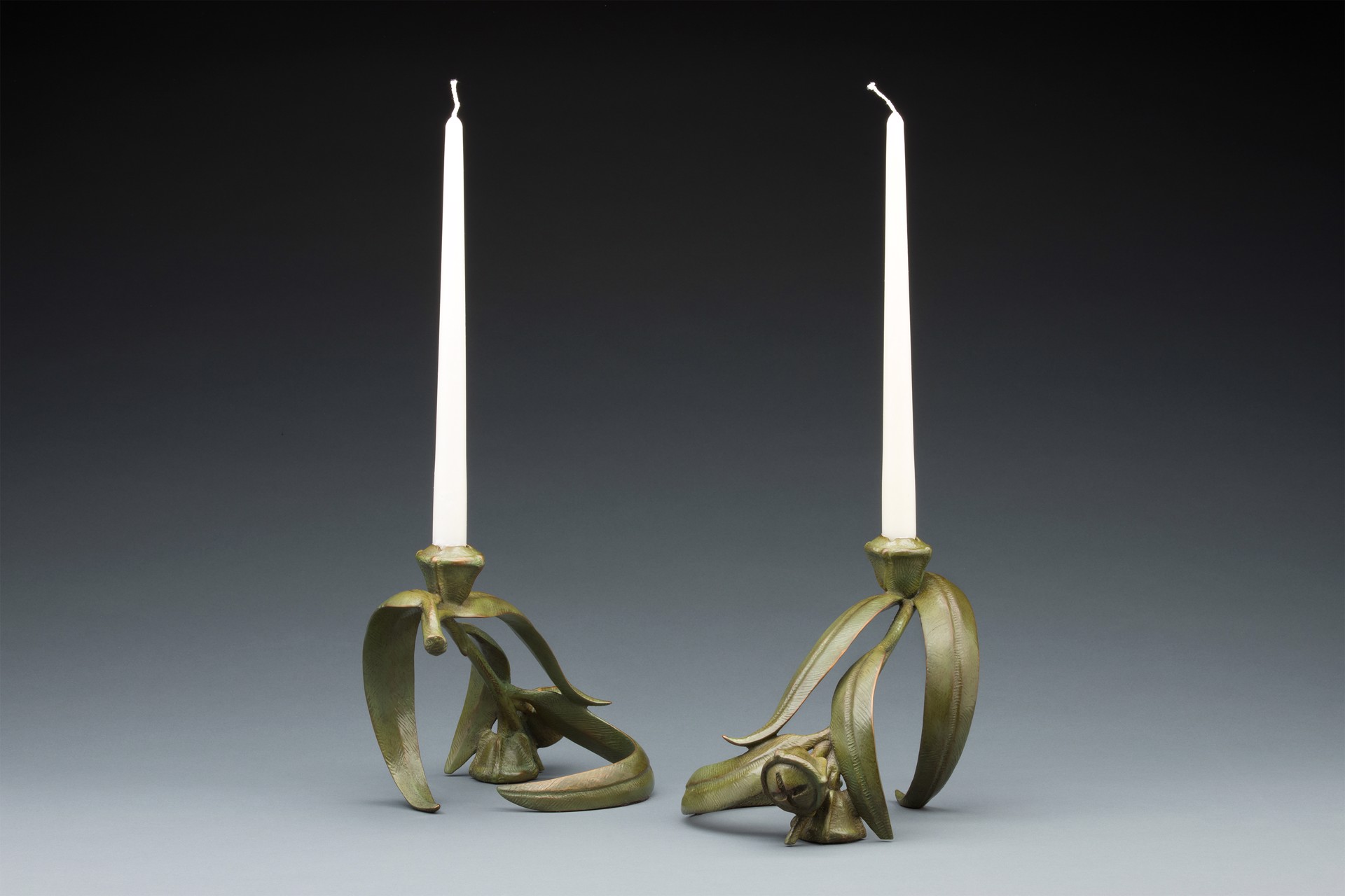 A pair of brass candlesticks with two white candles on them.