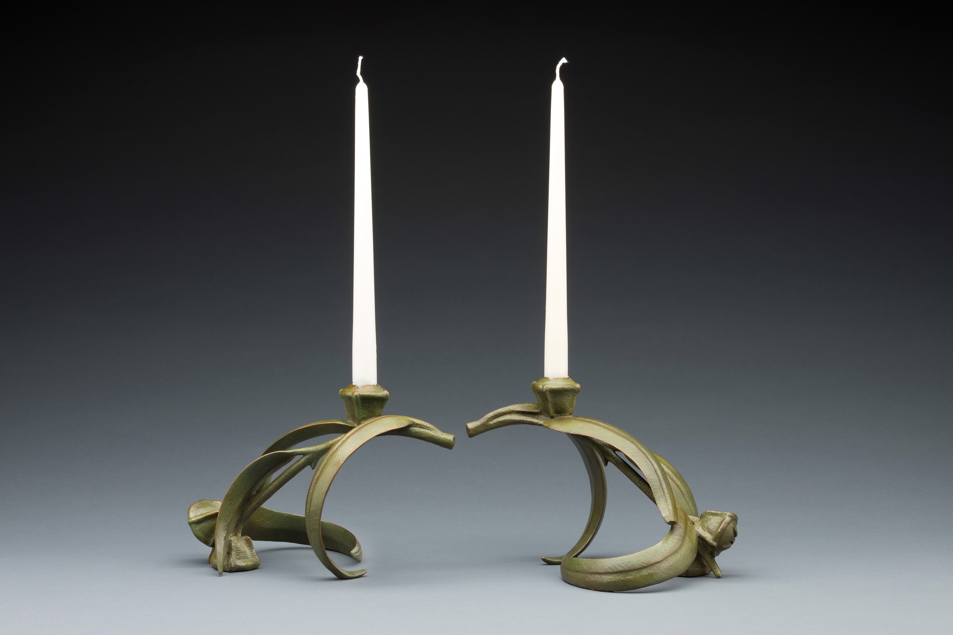 A pair of brass candlesticks with two white candles on them.