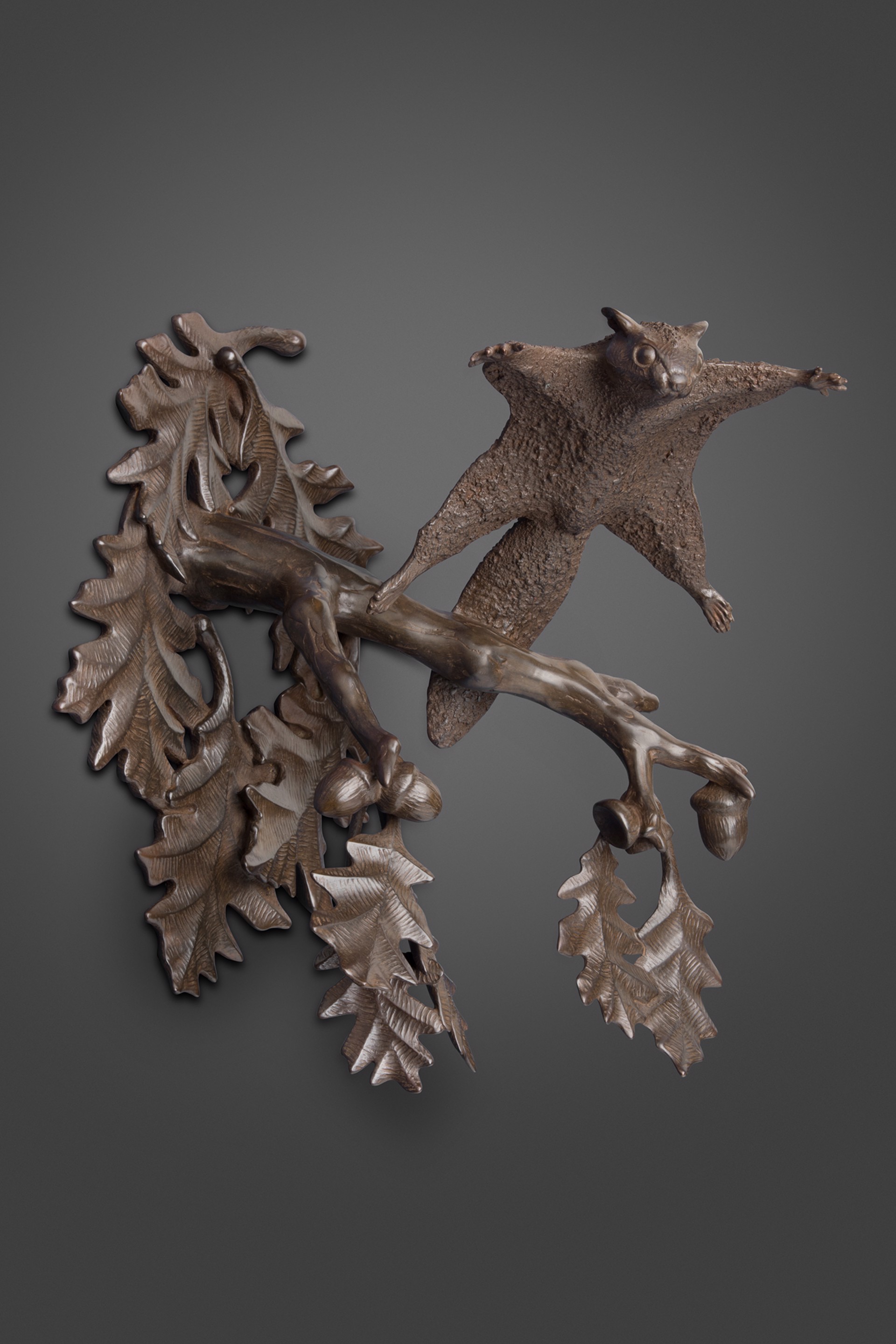 A bronze sculpture of a flying squirrel on a branch of oak leaves.
