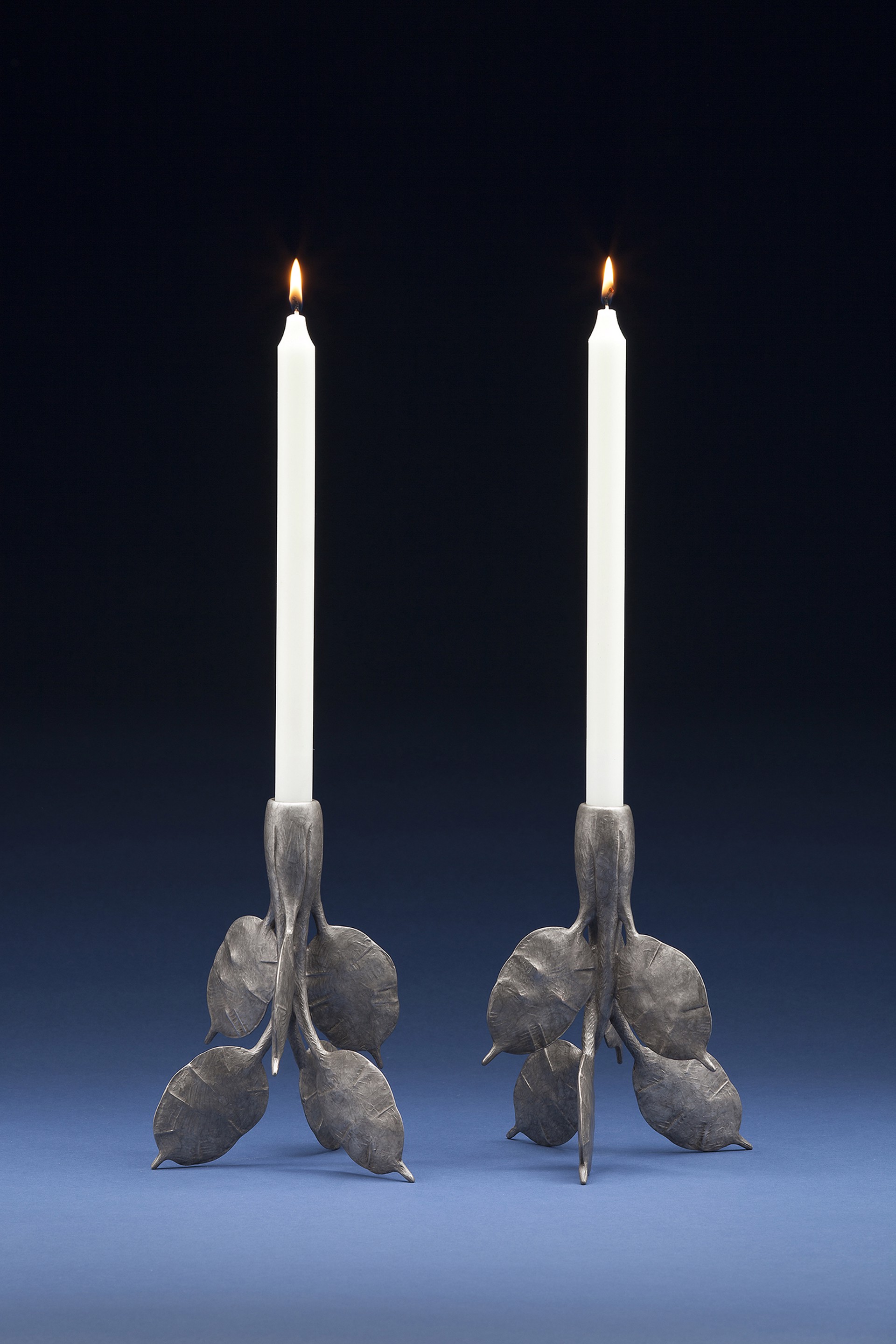 A pair of silver candlesticks with leaves on them. 
