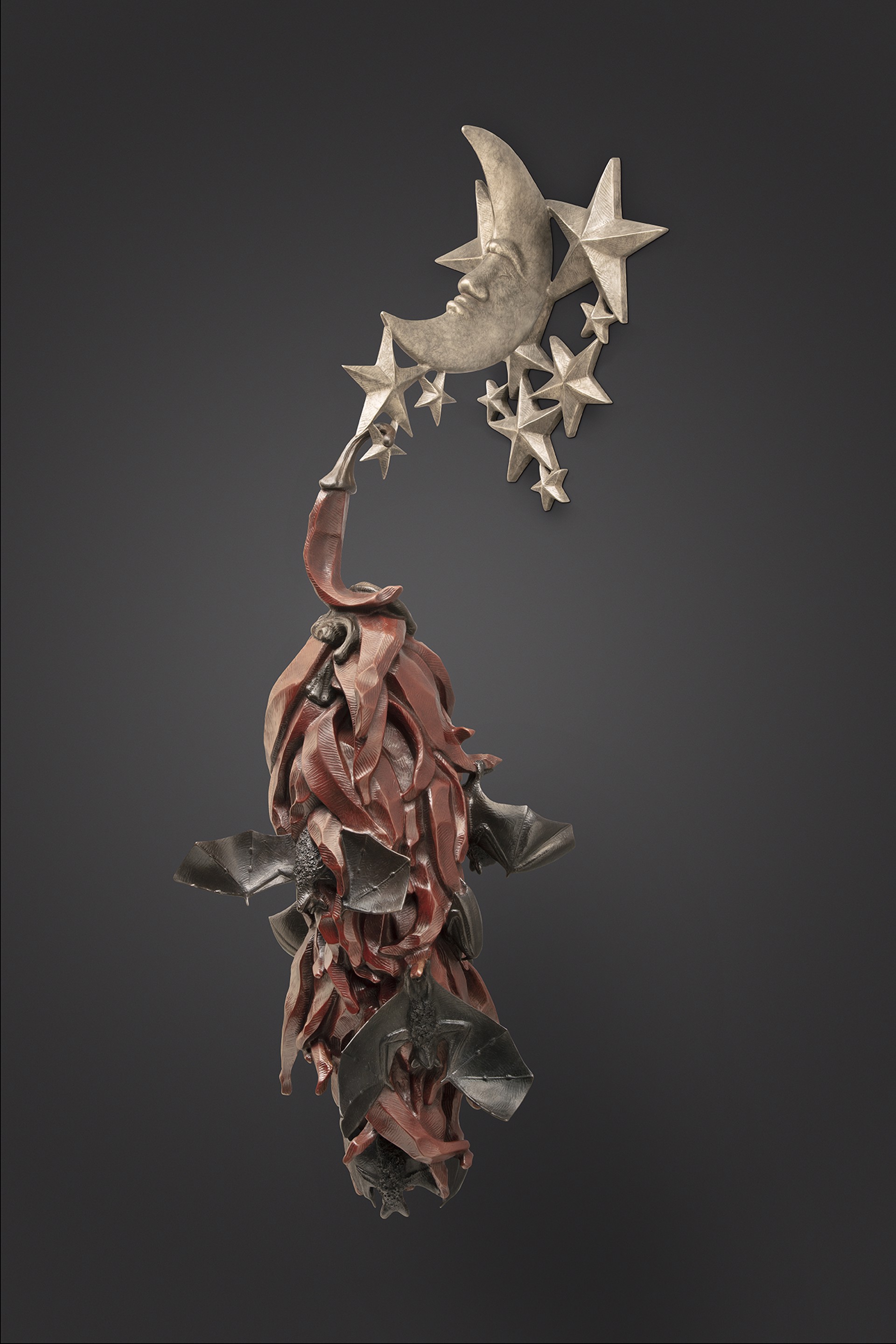 A surreal sculpture featuring a metallic crescent moon and stars suspended above a tangled mass of copper-colored ribbons.