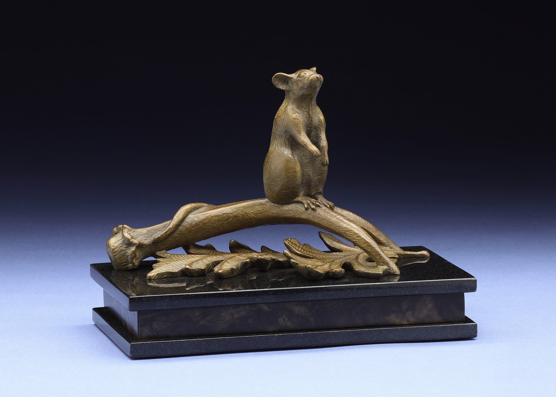 A bronze sculpture of a small rodent perched on a gnarled branch, resting on a dark rectangular base.