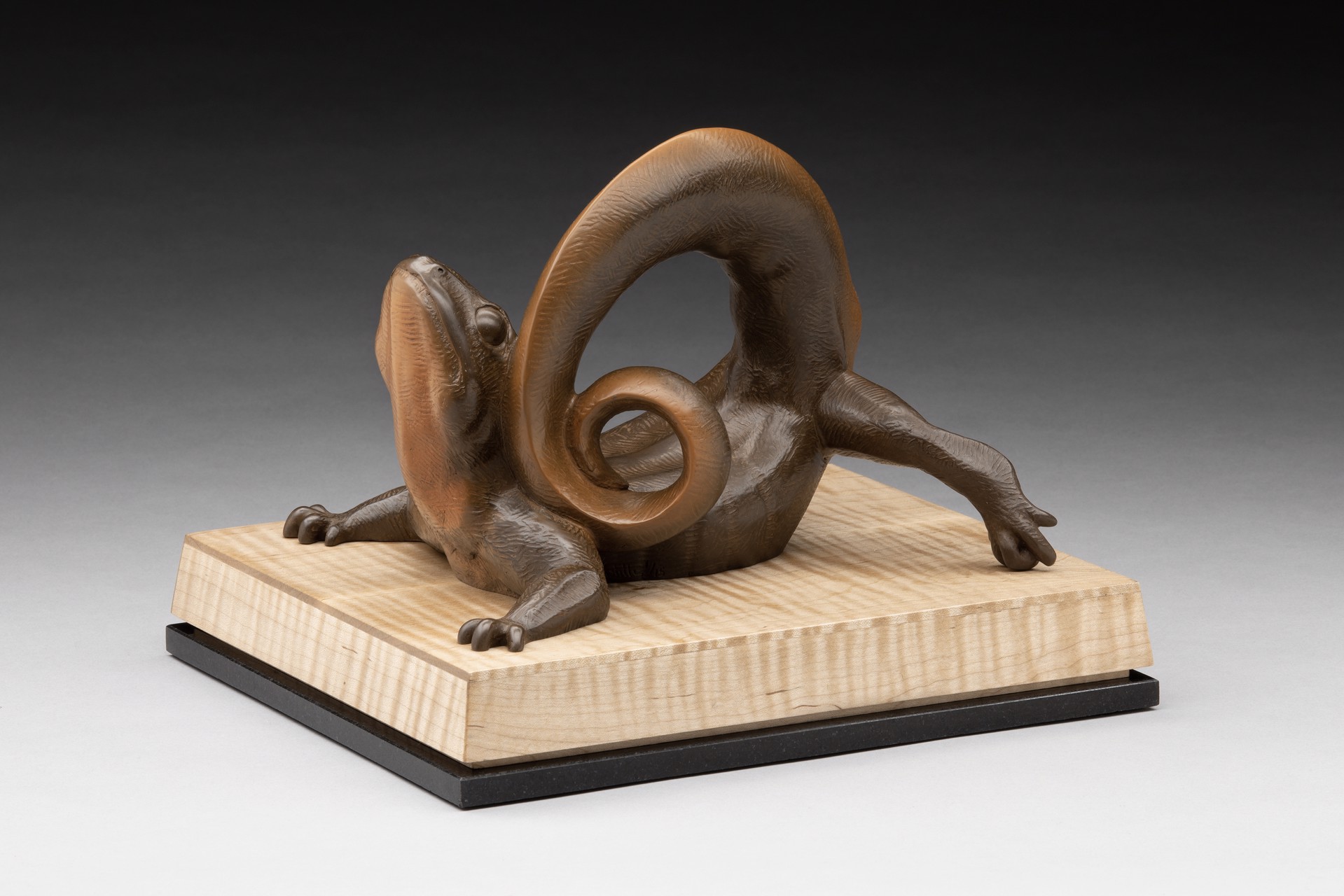 A bronze sculpture of a lizard on a wooden base.