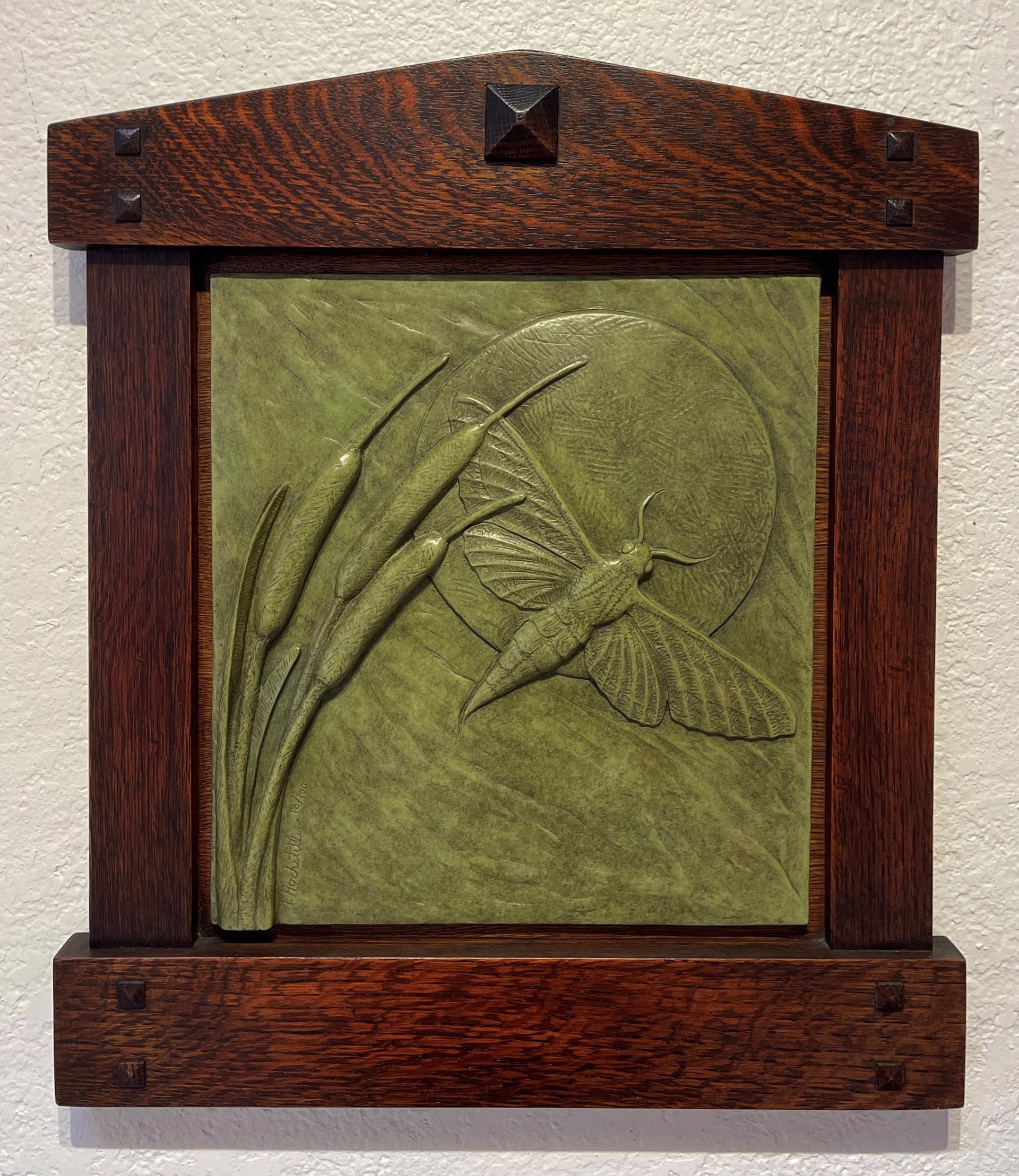 A relief sculpture of a moth and cattails in a wooden frame.