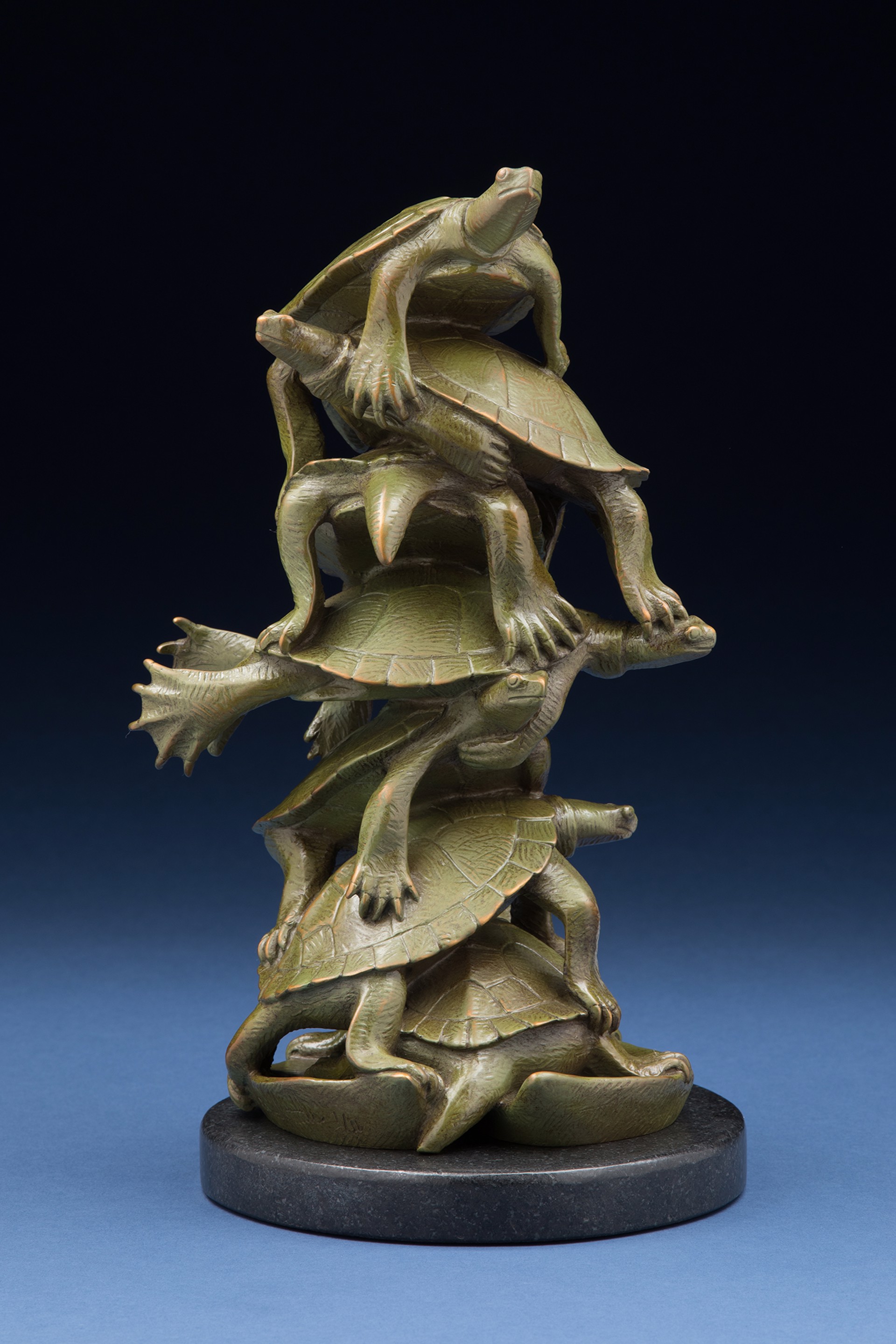 A bronze sculpture of stacked turtles forming a dynamic, upward-reaching composition.