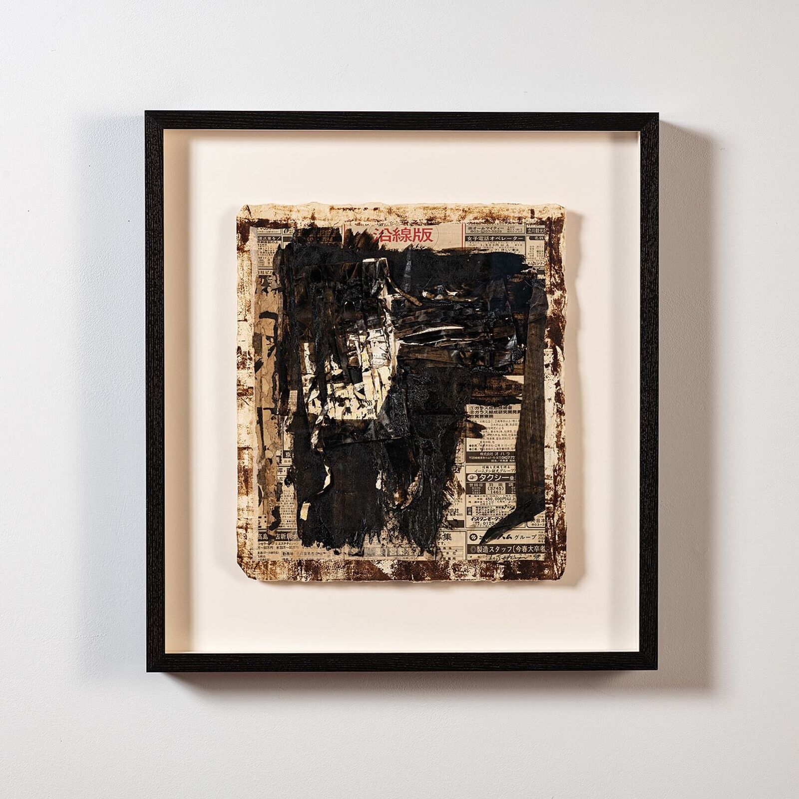 A framed mixed-media artwork featuring a dark, textured central form over a newspaper background.