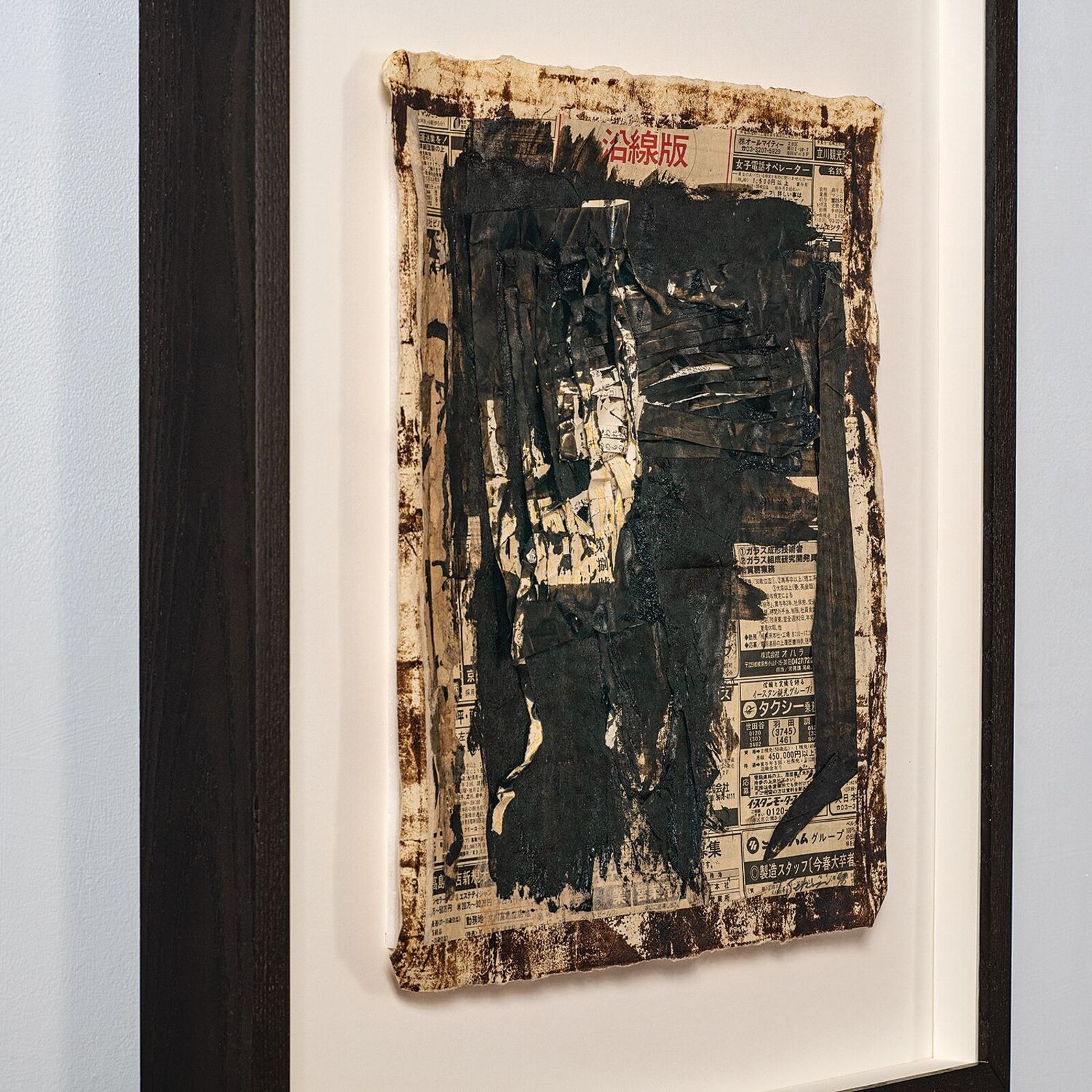 A framed mixed-media artwork featuring a dark, textured central form over a newspaper background.