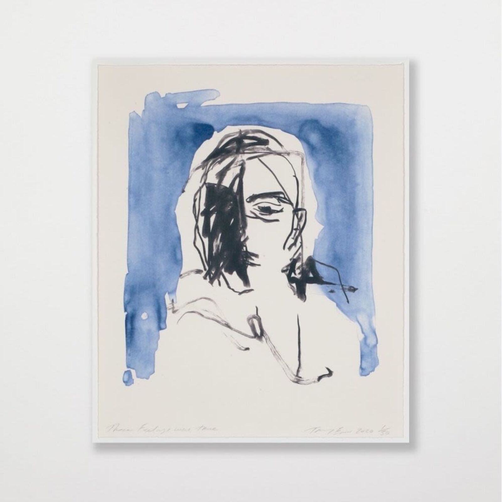A person in a pink top and wide-leg trousers stands observing a blue-toned portrait on a white gallery wall.