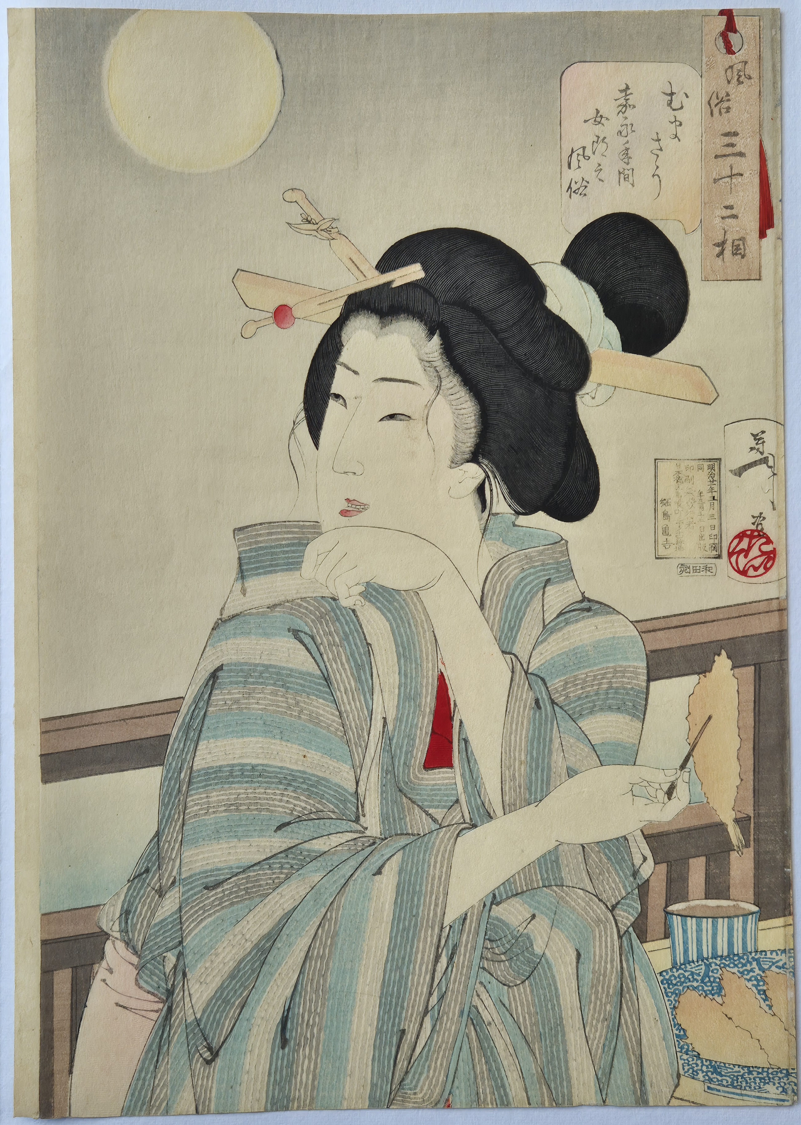 A woman in a kimono sitting at a table with chopsticks in her hair.
