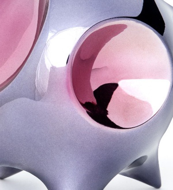 A glossy, abstract sculpture featuring a large reflective sphere and smooth, rounded forms in soft purple and pink tones.