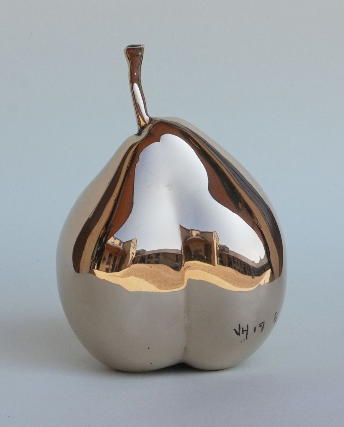 A polished metallic sculpture shaped like a pear, reflecting its surroundings.