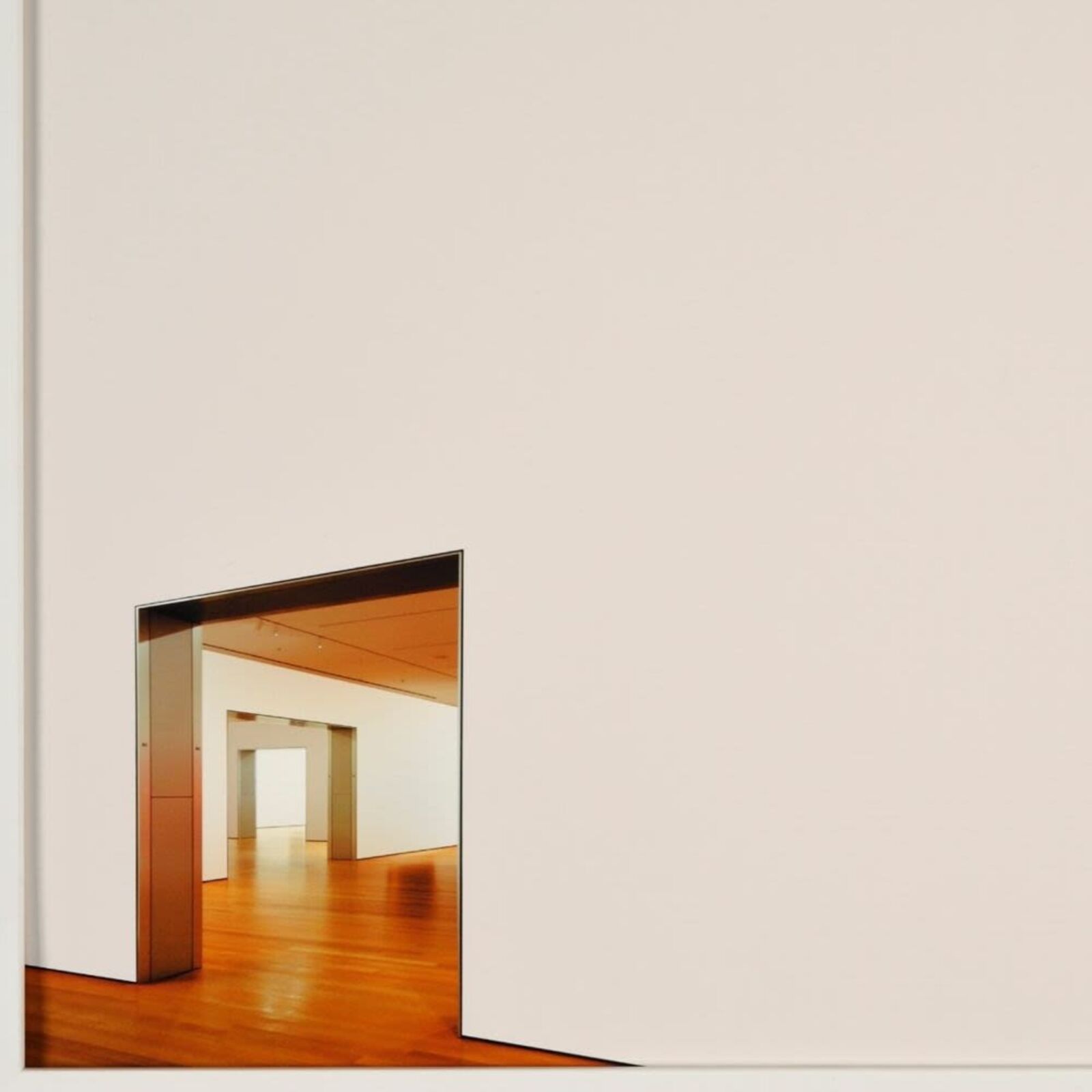 A minimalist framed photograph featuring a stark white wall with a small, colorful opening revealing an interior space.