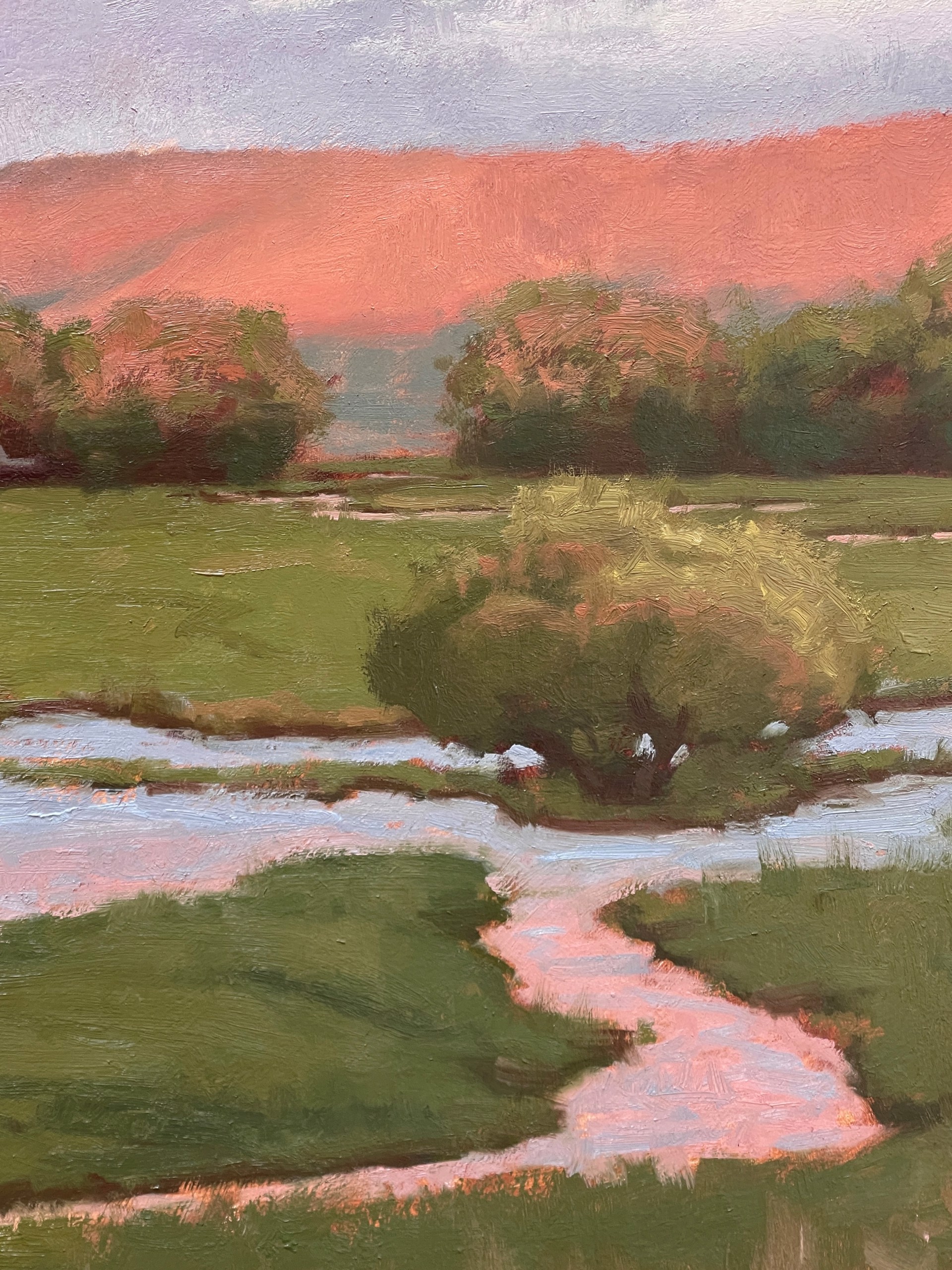 A serene landscape painting featuring a winding stream, green meadow, and dramatic pink clouds over distant hills.