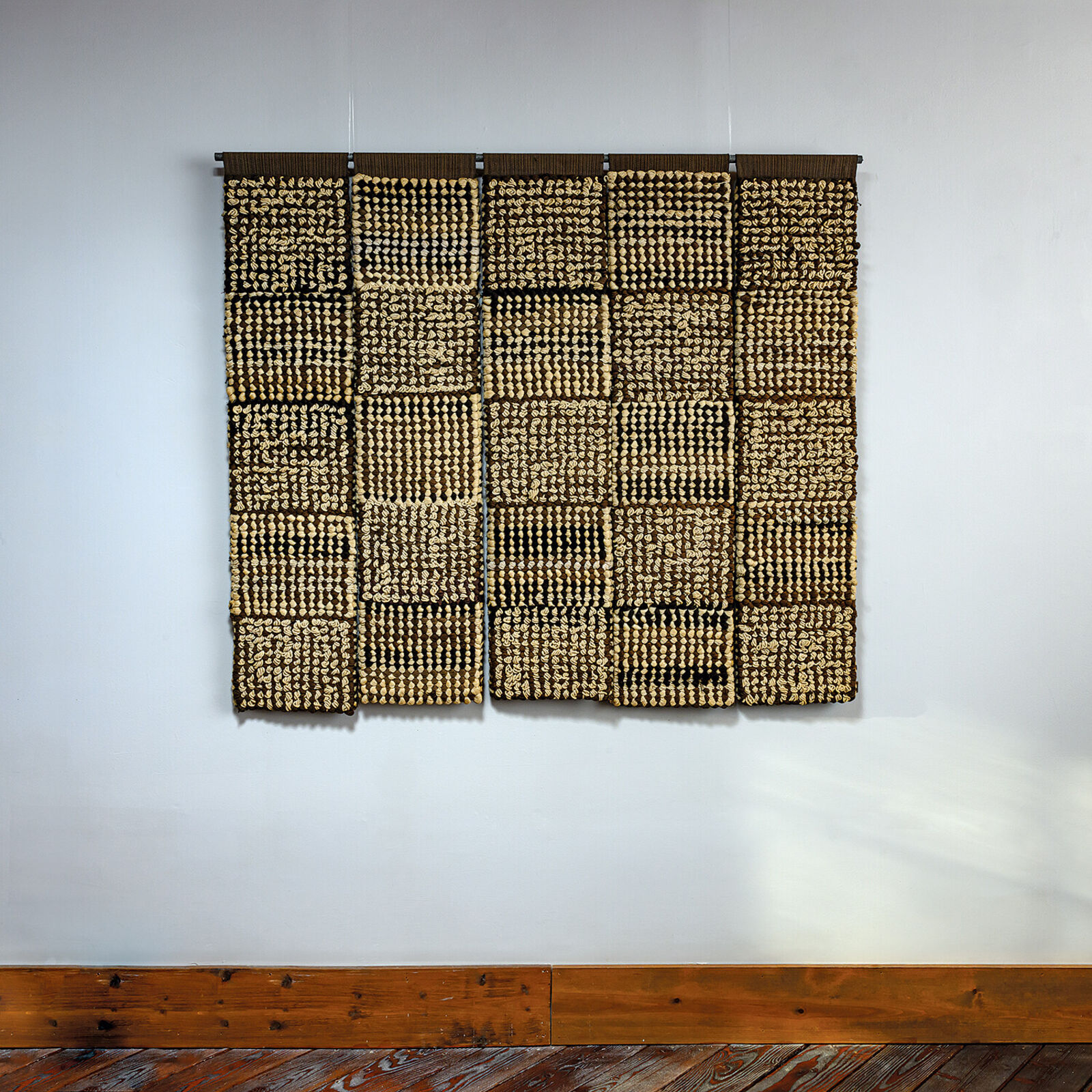 A woven textile artwork featuring a grid of textured squares in earthy tones.