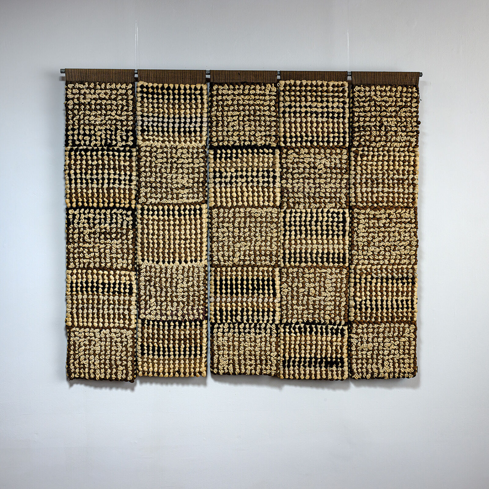 A woven textile artwork featuring a grid of textured squares in earthy tones.