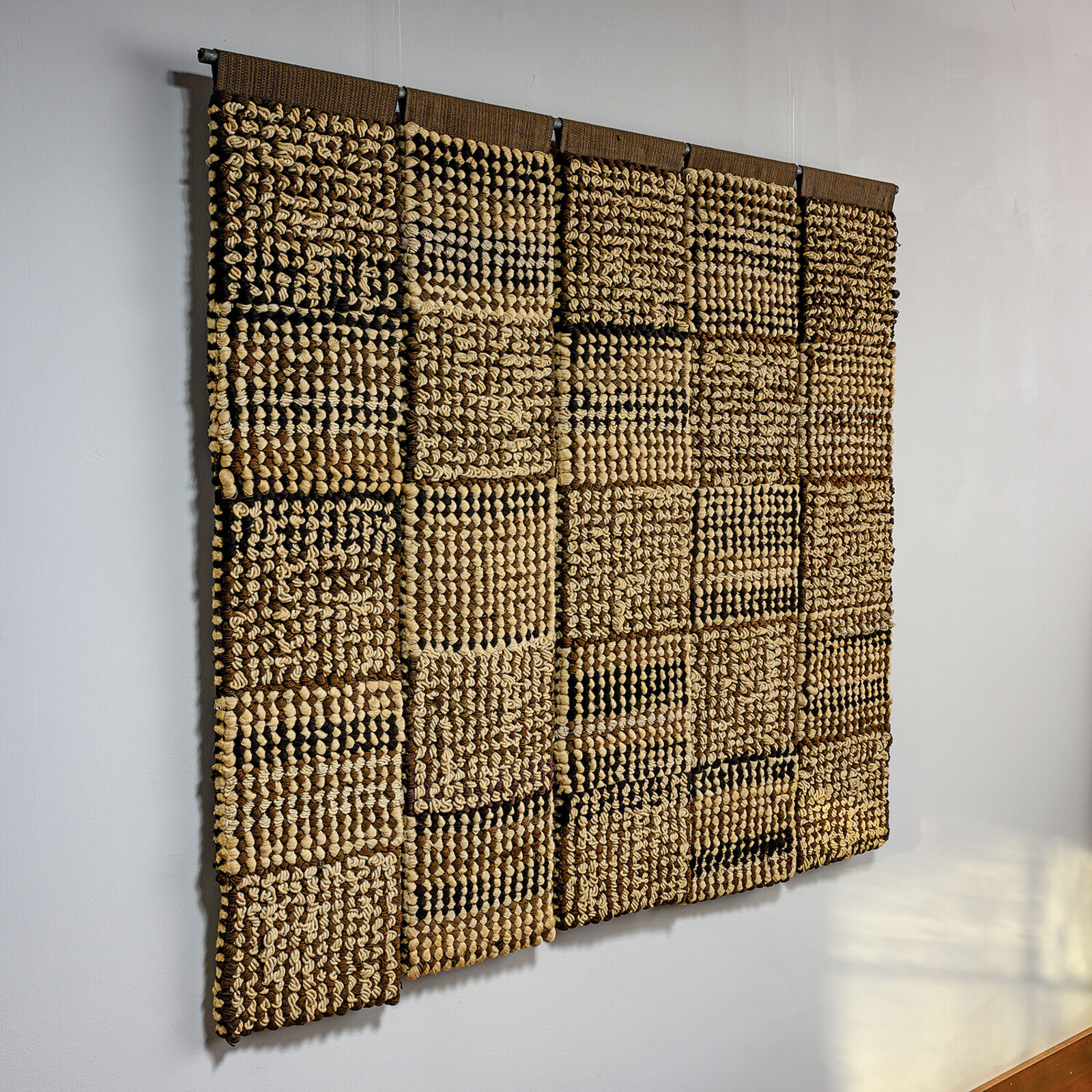 A woven textile artwork featuring a grid of textured squares in earthy tones.