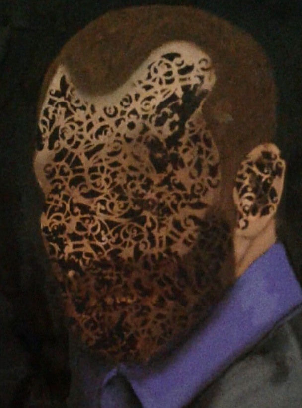 A portrait of a figure with an ornate lace mask covering the face, set against a dark background.