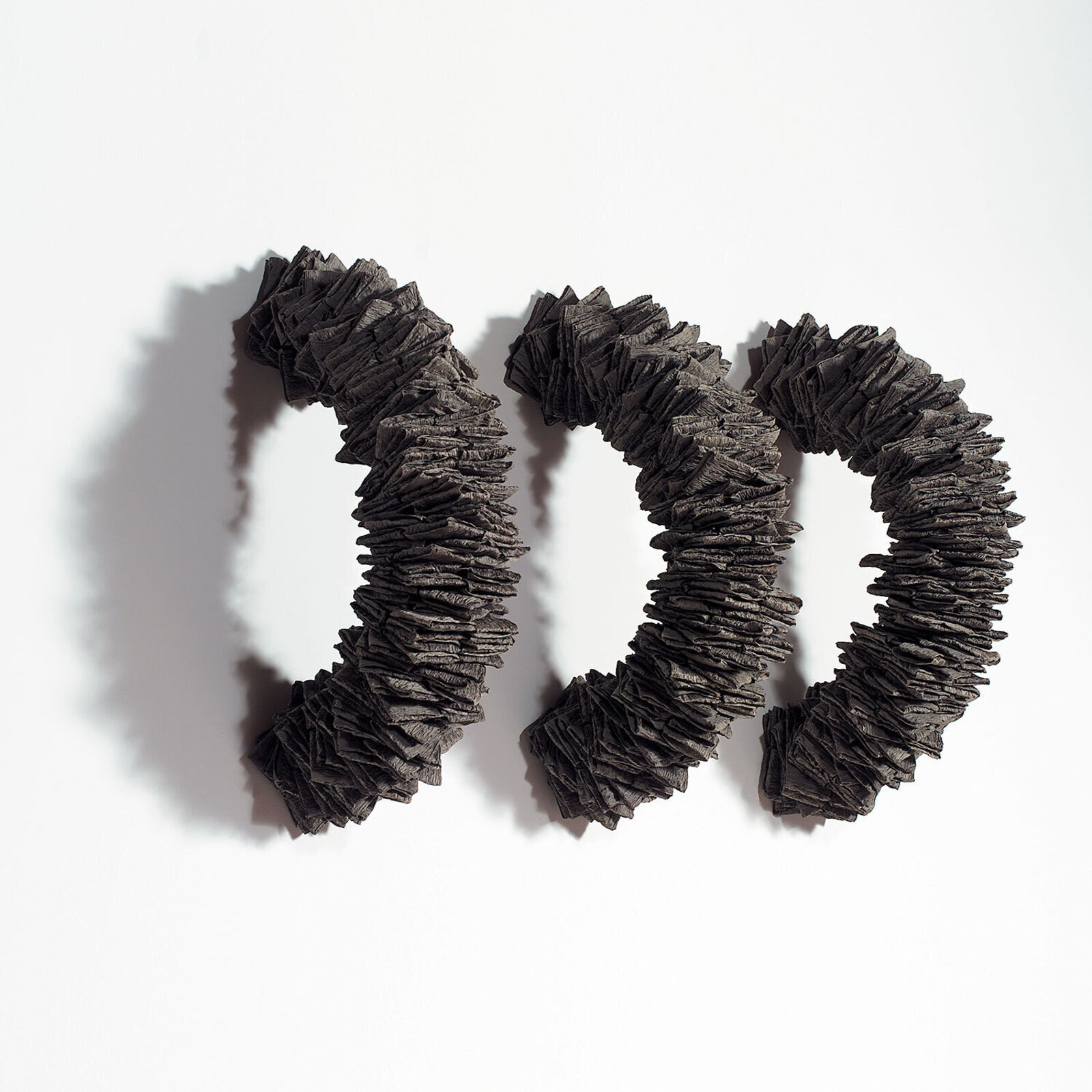 A minimalist composition featuring three dark, textured rings arranged in a diagonal line against a stark white background.
