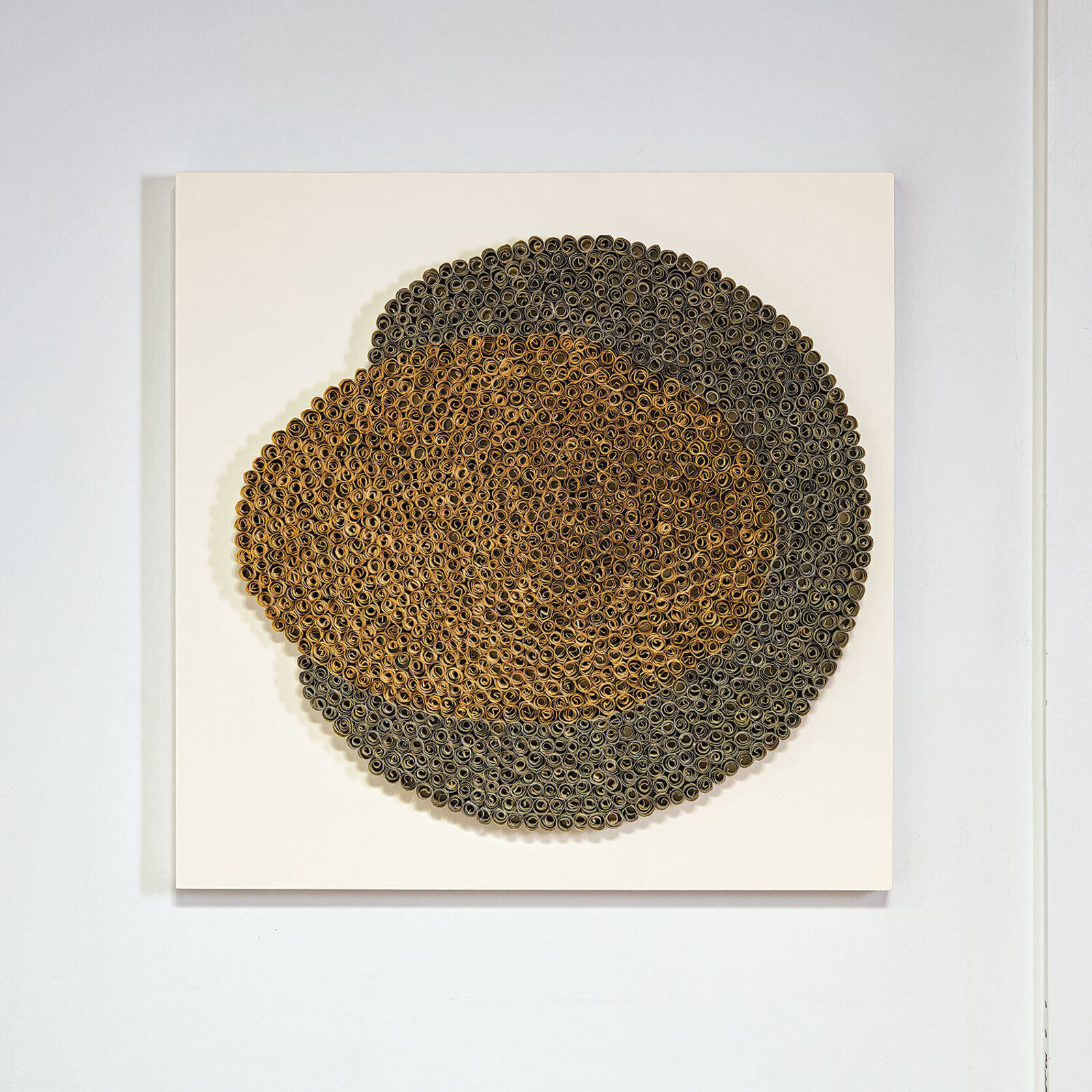 A textured circular artwork made of thousands of tiny rolled elements arranged in concentric rings.