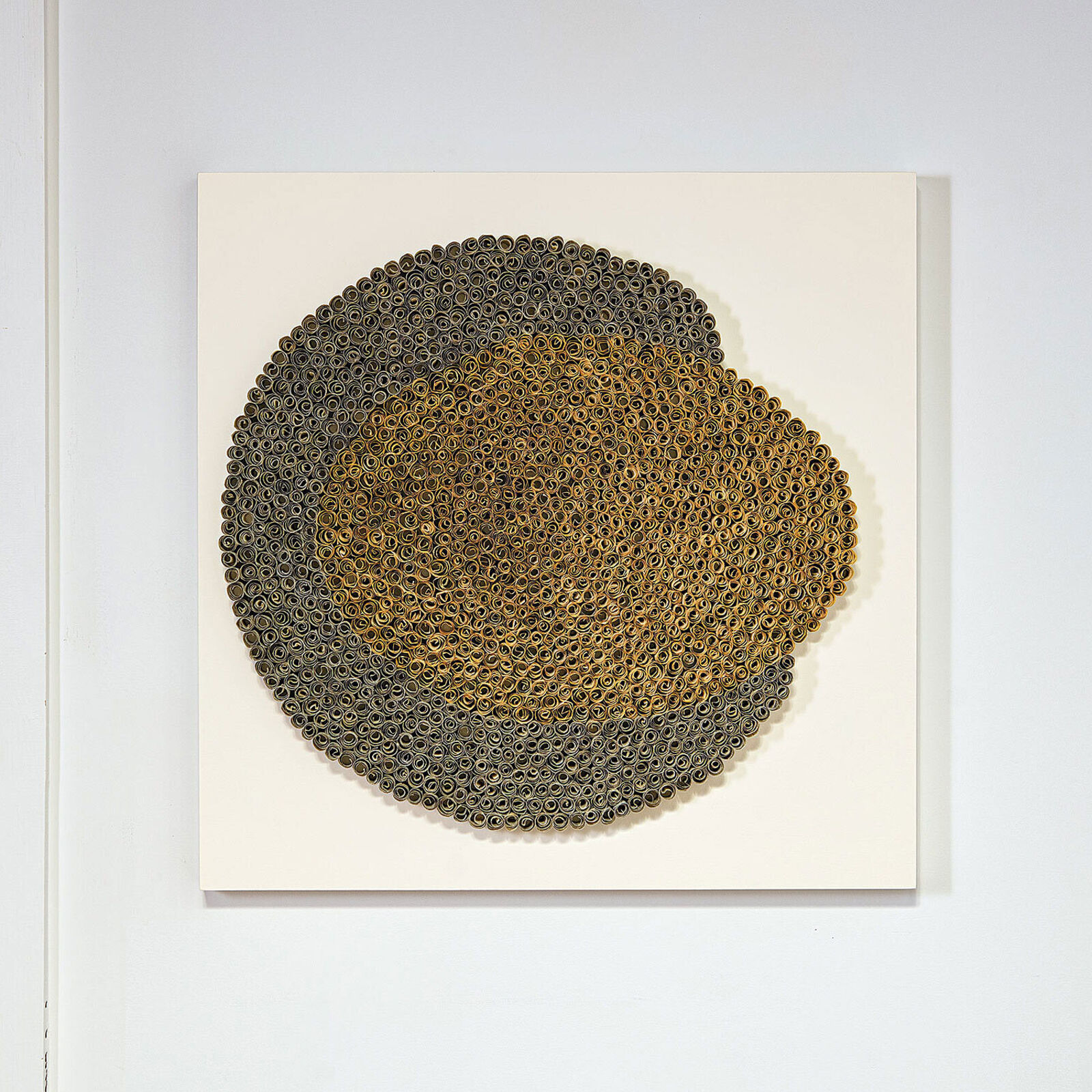 A textured circular artwork made of thousands of tiny rolled elements arranged in concentric rings.