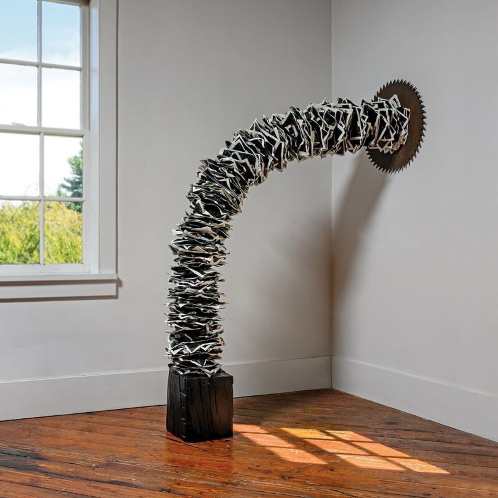 A sculptural installation featuring a jagged, metallic arch anchored by a dark block and ending in a spiked disc.