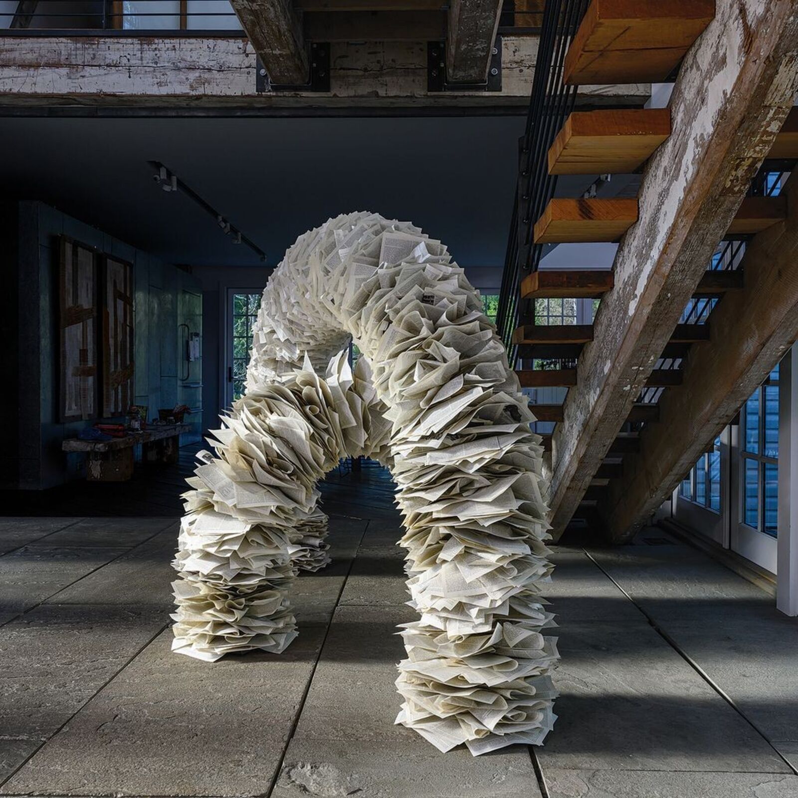A sculptural arch constructed from layered paper-like elements stands in a modern interior space.