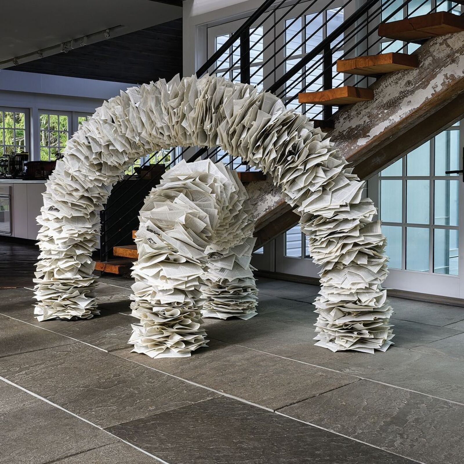 A sculptural arch constructed from layered paper-like elements stands in a modern interior space.