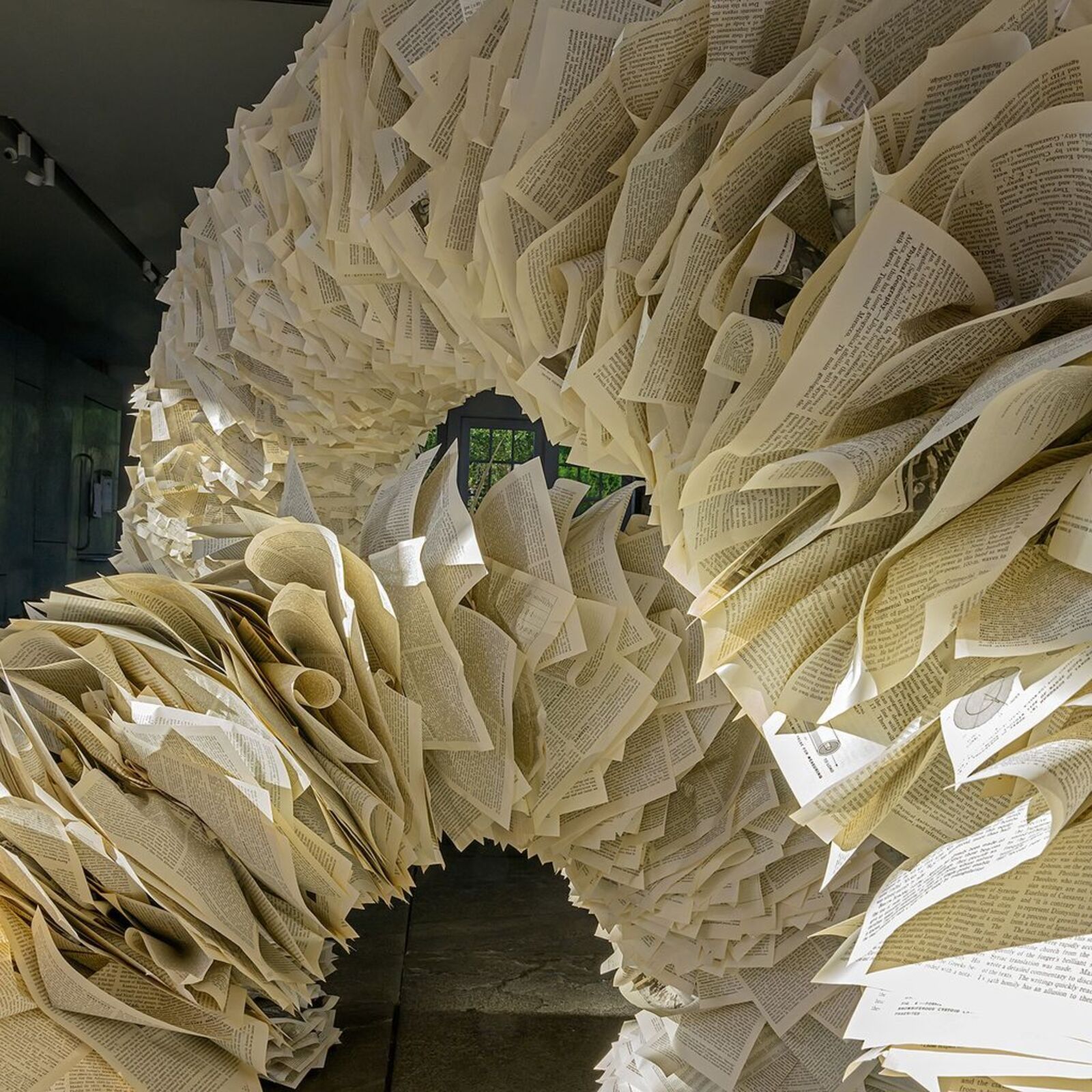 A sculptural arch constructed from layered paper-like elements stands in a modern interior space.