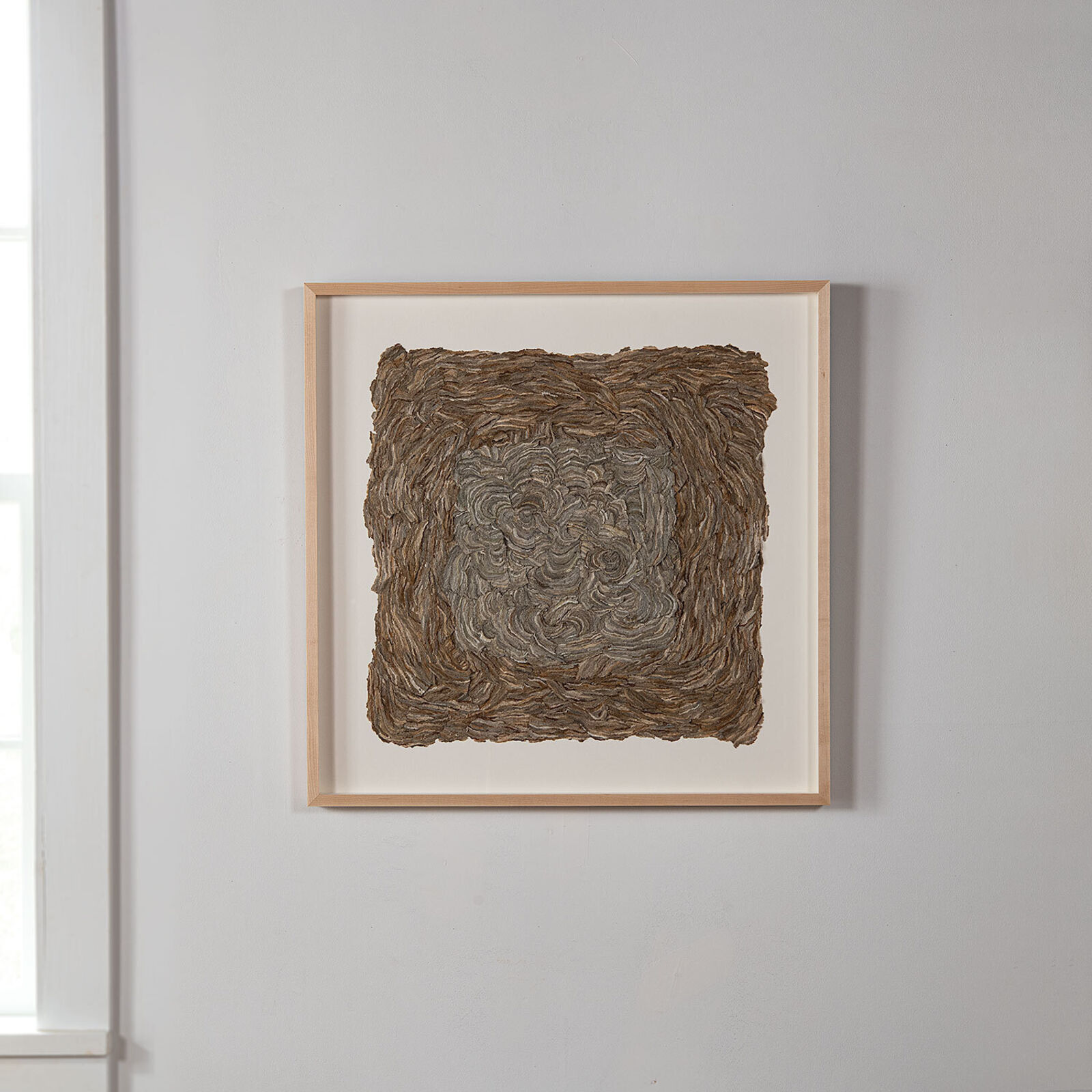 A framed square artwork featuring a textured, swirled surface in earthy tones.